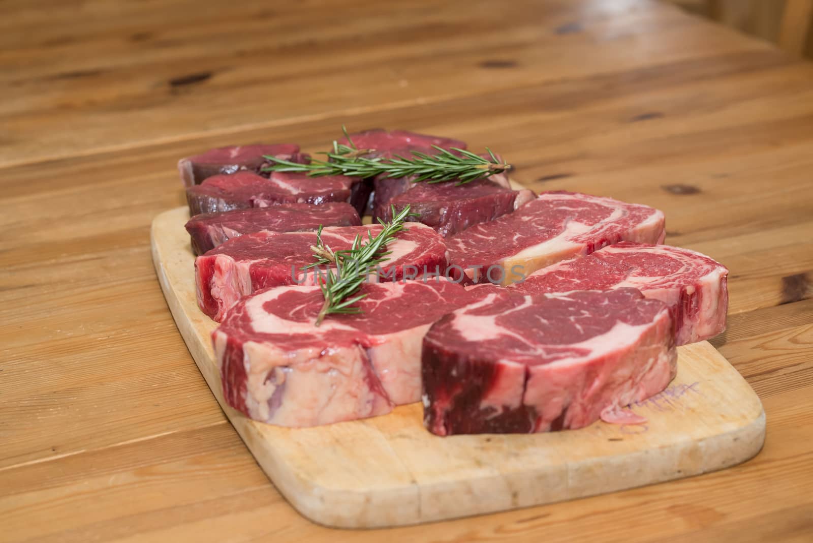 Raw steaks on a cutting board garnished with herbs