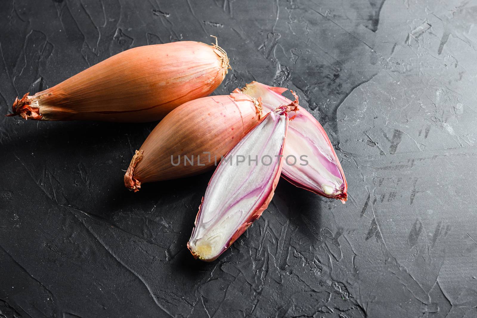 Shallot, eschalot or scallion raw ripe onions sliced and halved black concrete textured background top view space for text.
