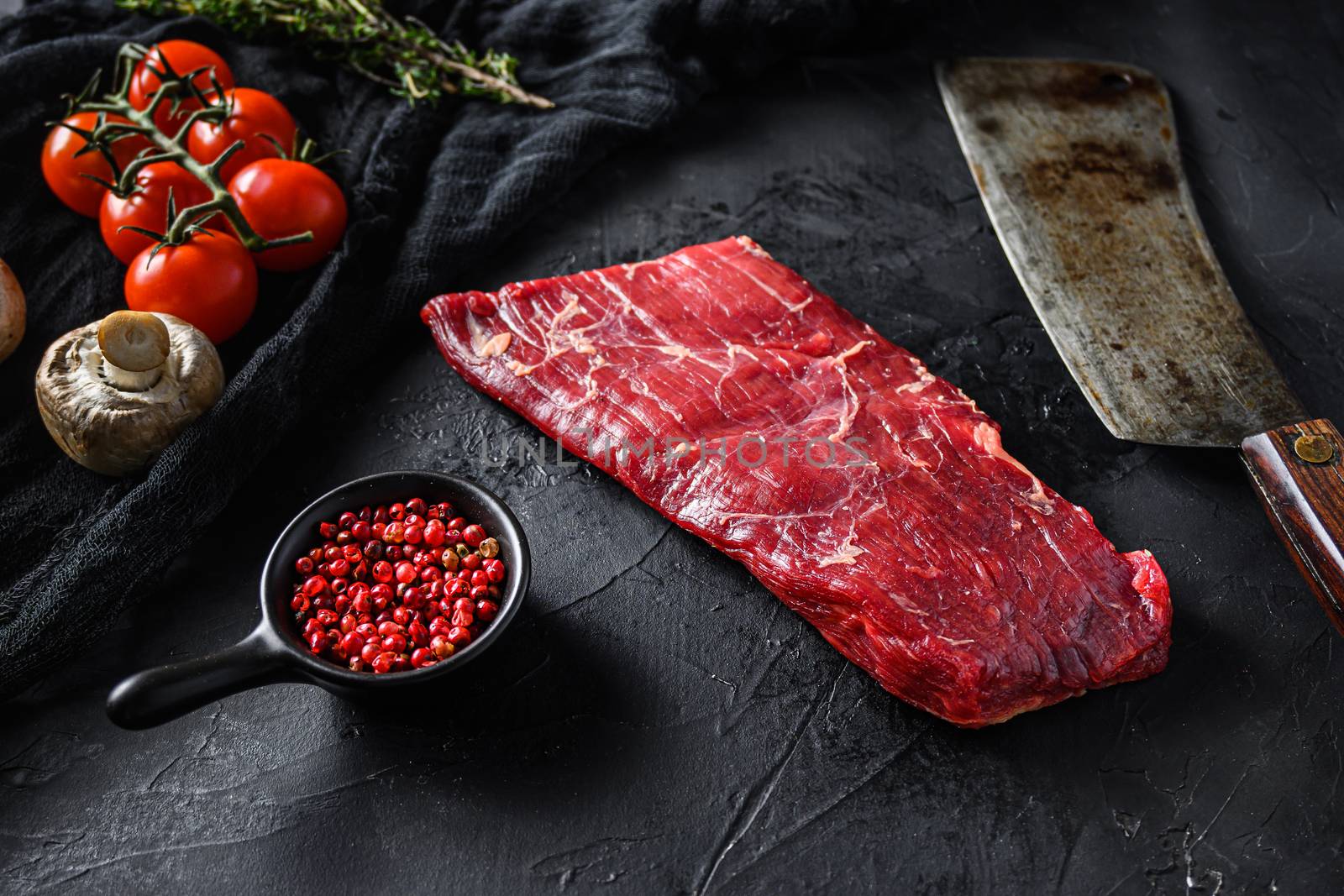 Raw, flap or flank, also known Bavette steak near butcher knife with pink pepper and rosemary. Black stone background. Side view vertical by Ilianesolenyi