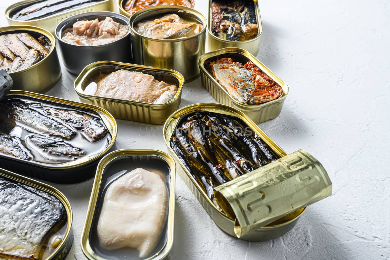Opened preserve cans with Saury, mackerel, sprats, sardines, pilchard, squid, tuna over white textured stone table side view space for text.