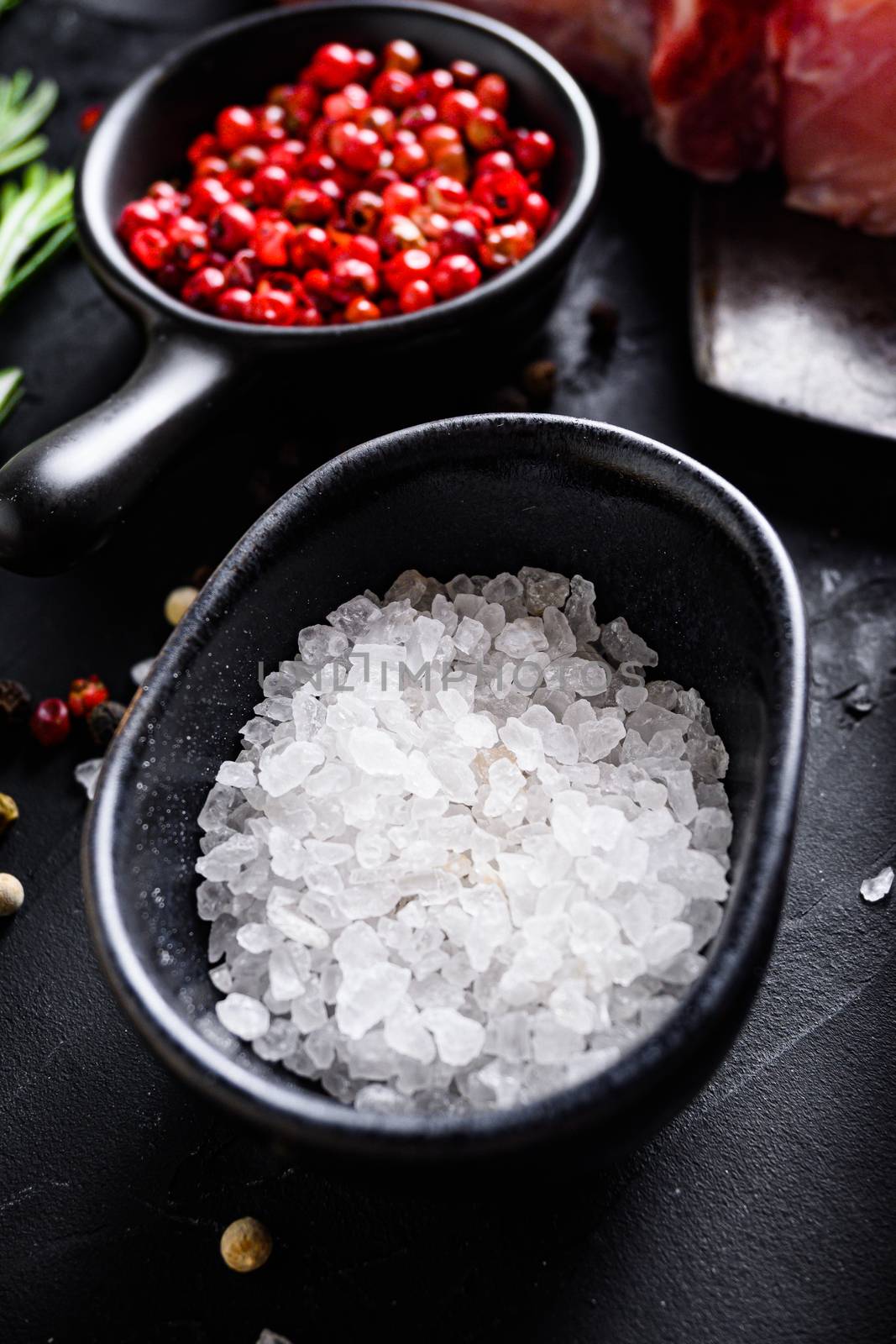 Sea Salt in black bowl and Rosemary herbs close up on black stone table with spices and raw meat near side view selective focus vertical by Ilianesolenyi