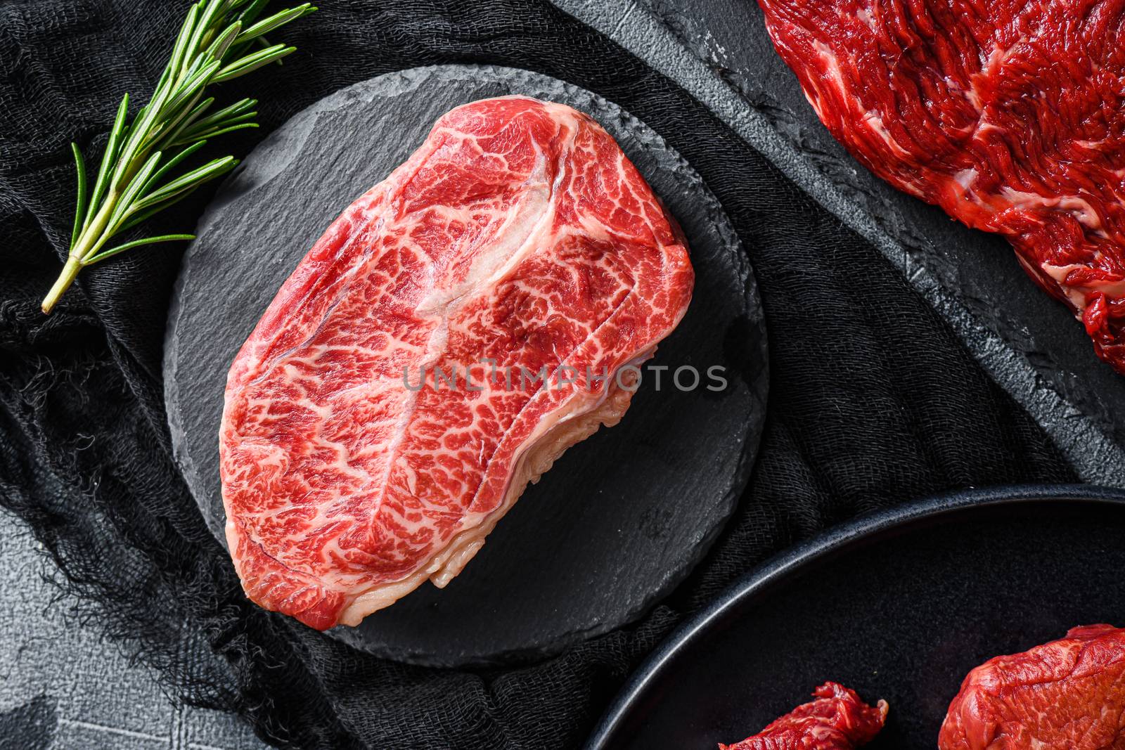 Raw top blade cut black angus organic steak on a black plate and stone slate with seasonings, herbs grey concrete background. Top view close up. by Ilianesolenyi