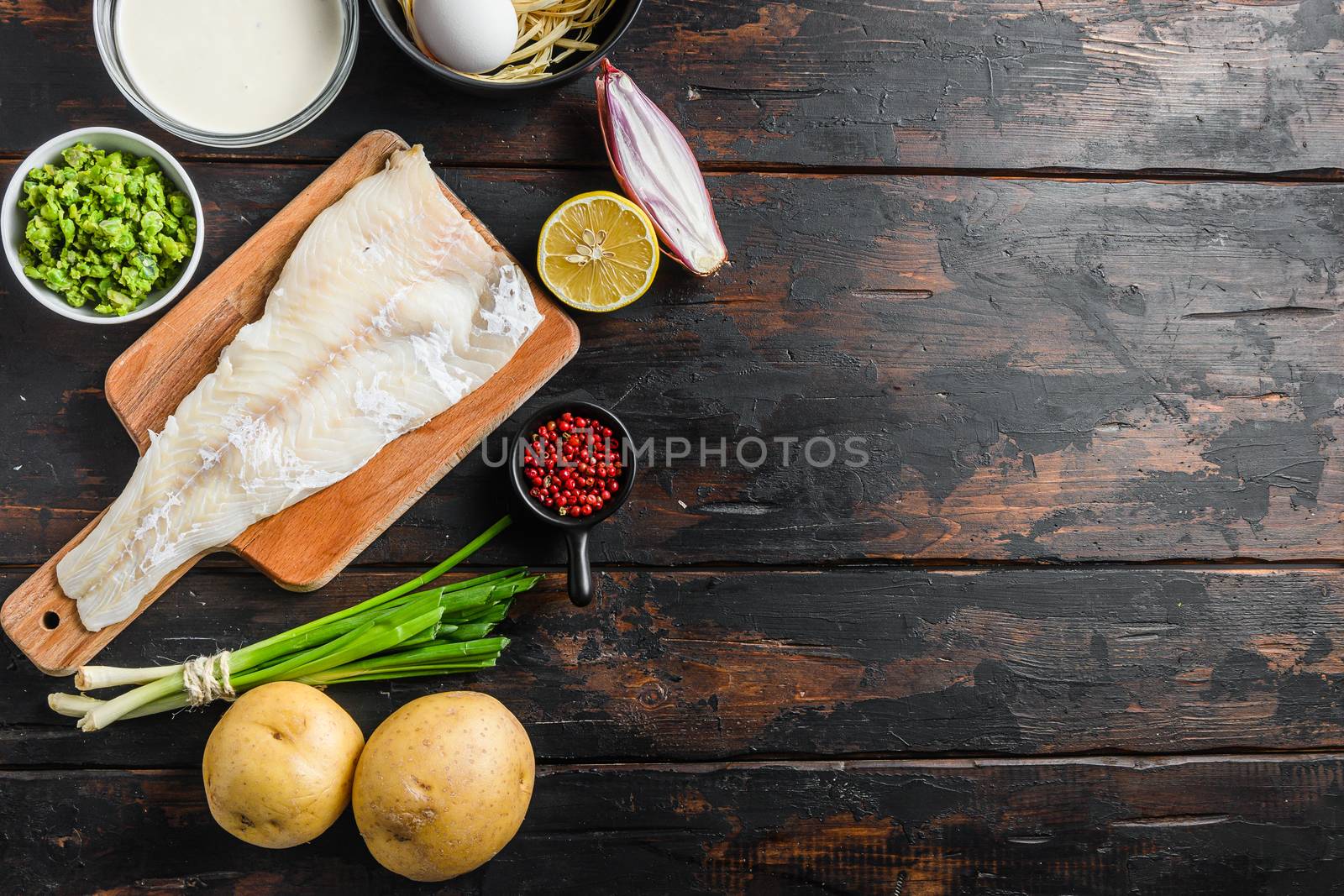 Raw organic Cod fillet fish and chips ingredients beer batter, potatoe, tartar sauce, minty mushy peas, lemon , shallot, mint, garlic, salt, peppercorns on rustic old wood table top view space for text. by Ilianesolenyi