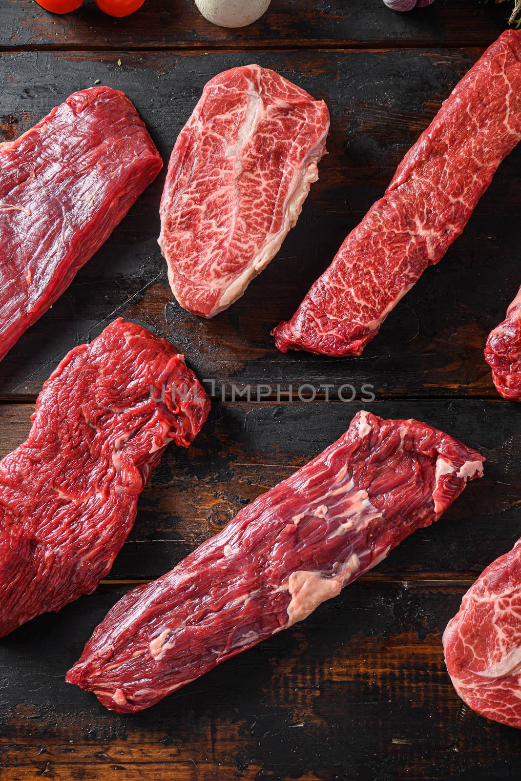 Alternative beef cut machete skirt steak close up in front of other cuts in butchery on old wood table top view vertical.