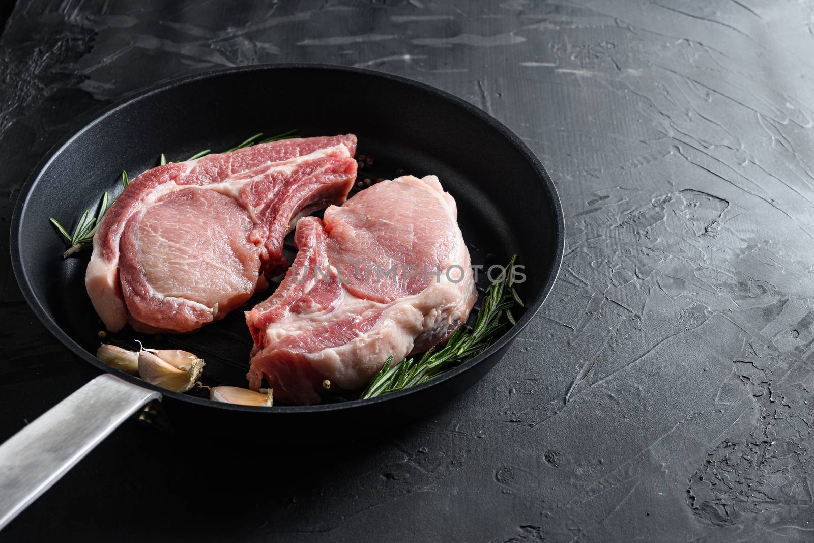 pork rib chops in frying pan grill skillet with herbs, spices side view black stone bakground space for text vertical.