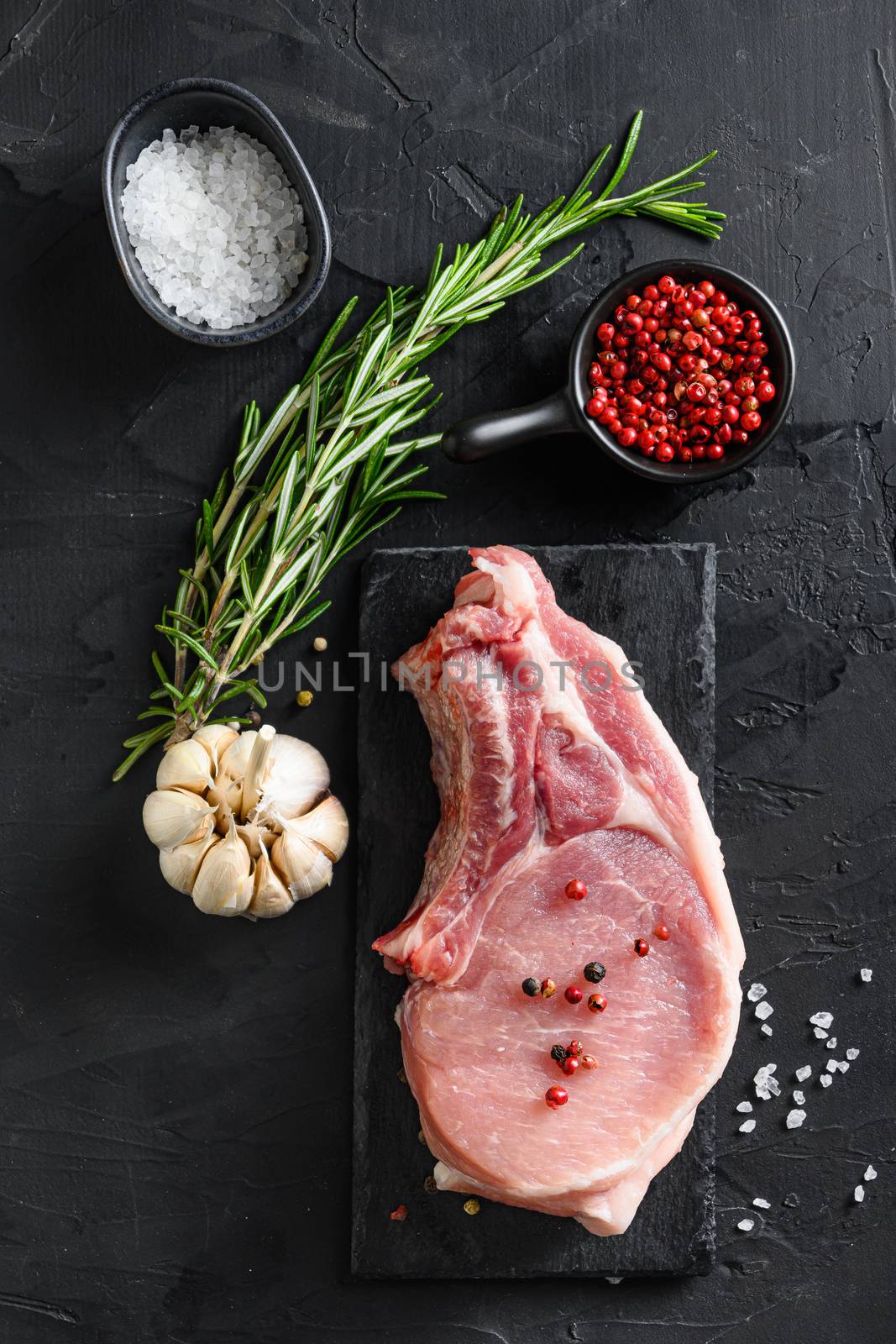 Porco Iberico French Rackswith salt and garlic, pepper on black slate stone board with rosemary, and fresh ingredients for grill over black textured background top view, flatlay on a black stone background vertical by Ilianesolenyi