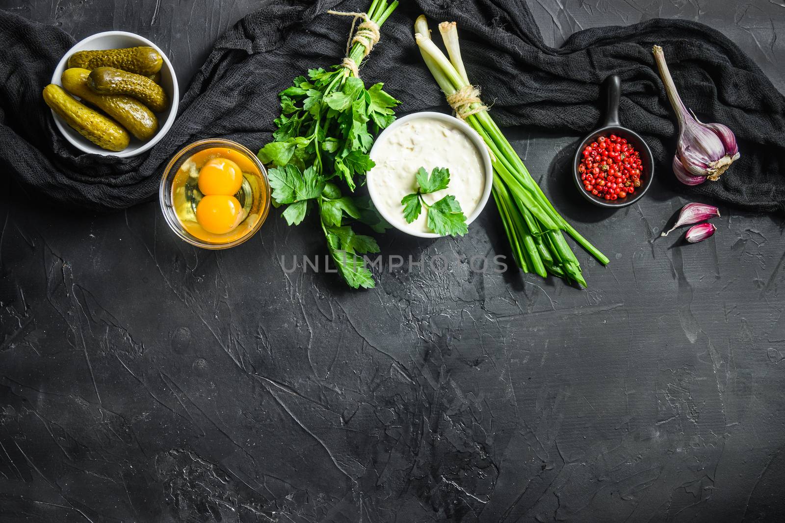 Ranch sauce organic bio tartare in a white porcelain bowl with vegetables, herbs and spices on old textured black stone table top view horisontal concept space for text in bottom.
