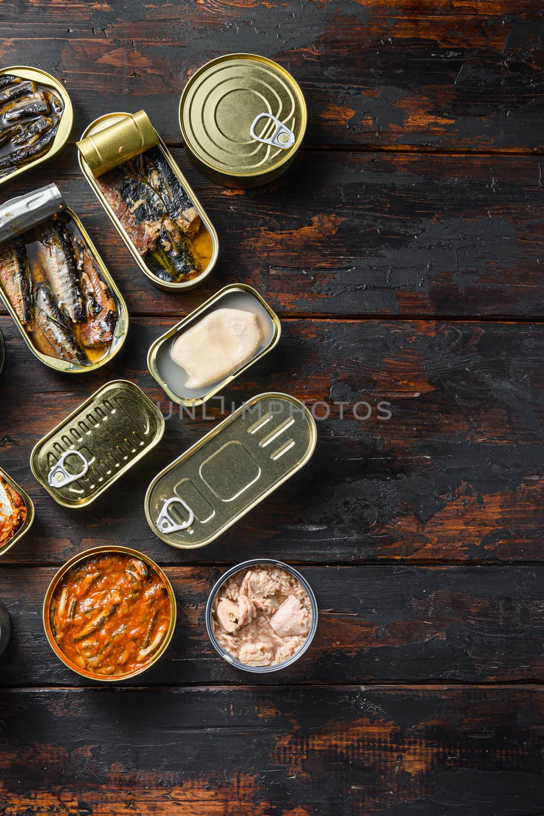 Tin cans for fish with different types of seafood, opened and closed cans with Saury, mackerel, sprats, sardines, pilchard, squid, tuna, over dark wood old table flat lay top view space for text vertical concept.