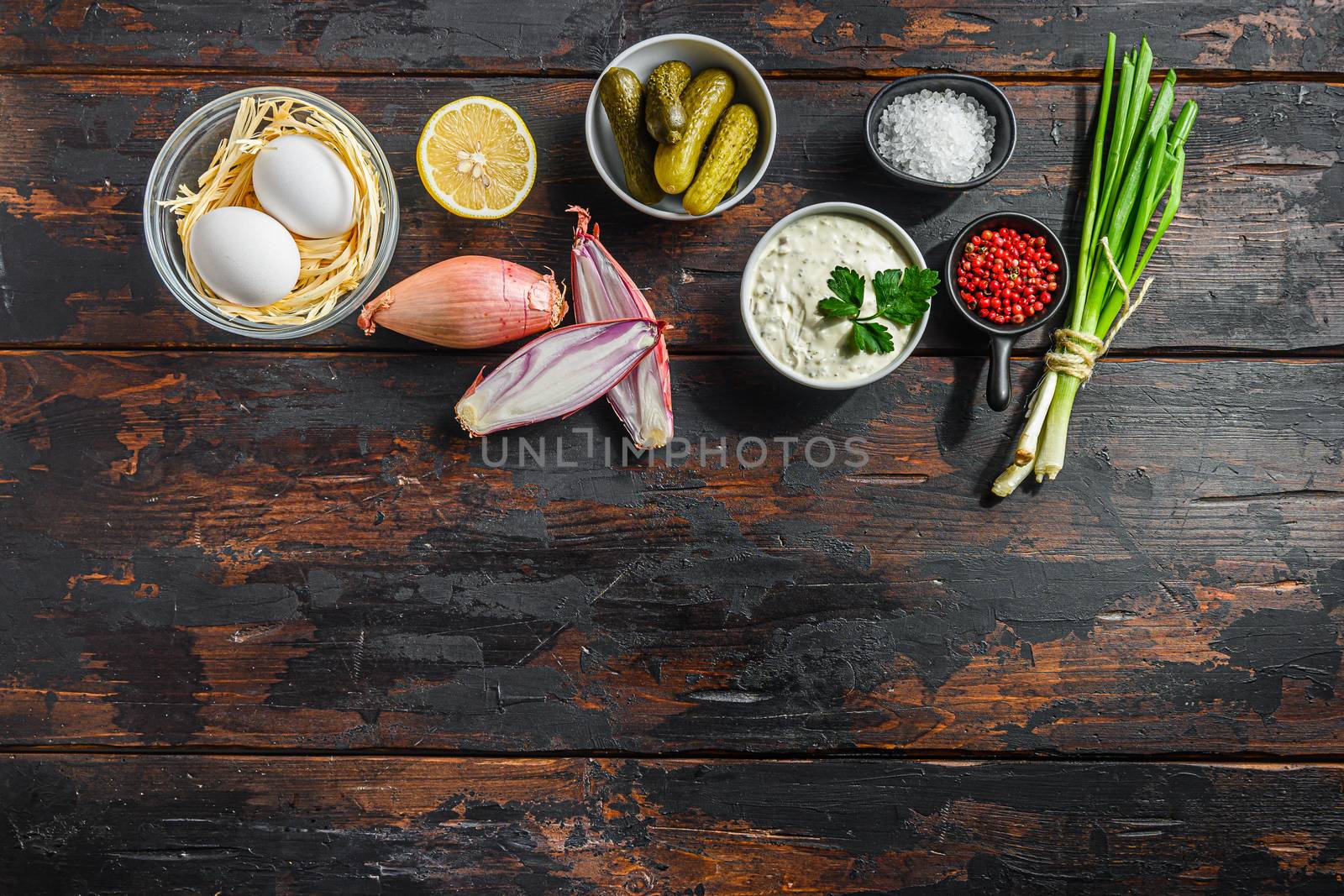 Organic tartar ingredients in a row pickles, capers, dill, parsley, garlic, lemon over old wood table and space for text concept on bottom by Ilianesolenyi