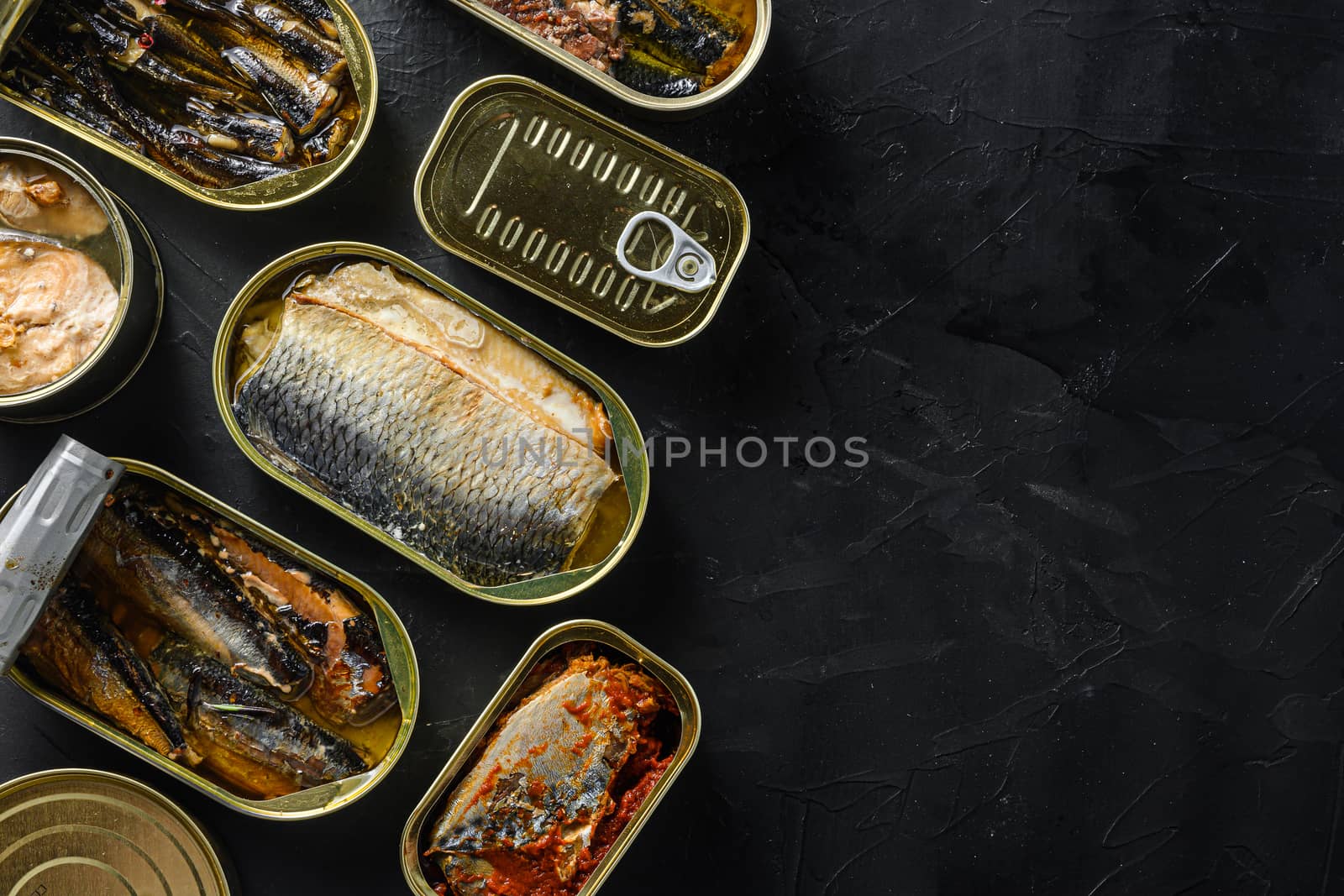 Saury, mackerel, sprats, sardines, pilchard, squid, tuna, Canned fish in tin cans. Open and closed over black slate background top view space for text.