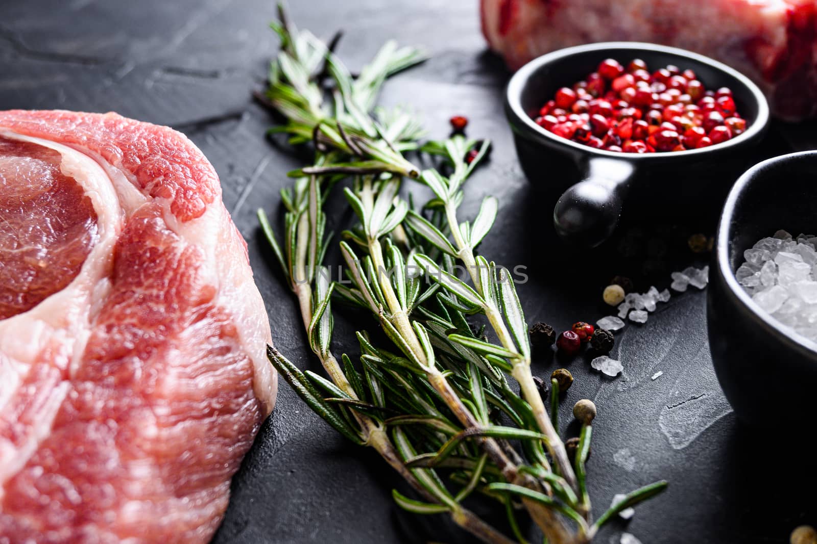 Rosemary herbs close up on black stone table with spices and raw meat near side view selective focus.