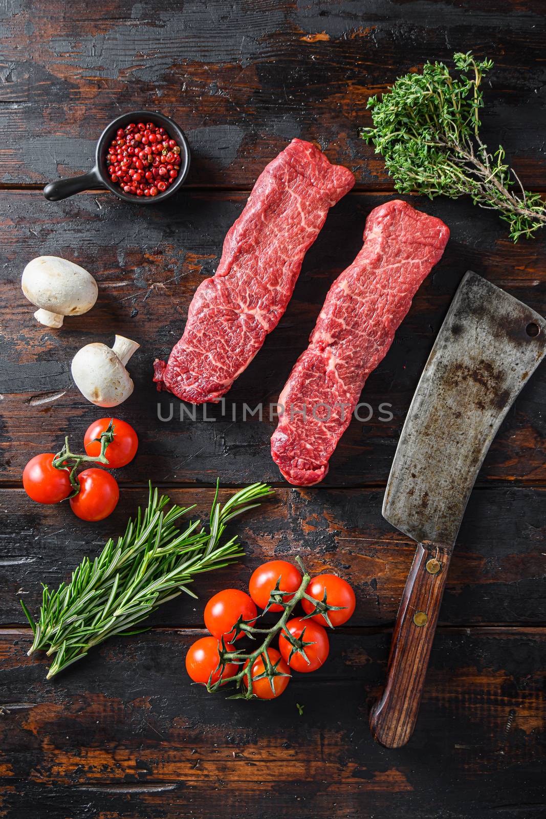 Organic denver steak, raw meat, marbled black angus beef cut on metal butcher cleaver knife with rosemary and farm herbs over old wood table background top view .