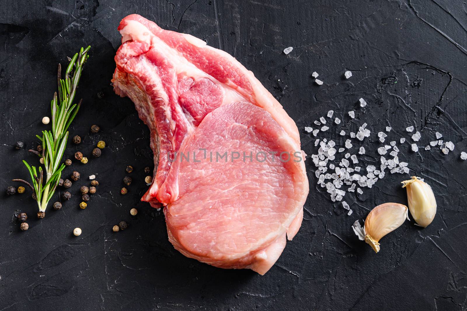 Organic chop on a bone or Pork belly fresh raw meat with spices and rosemary and red pepper on black slate top view. by Ilianesolenyi