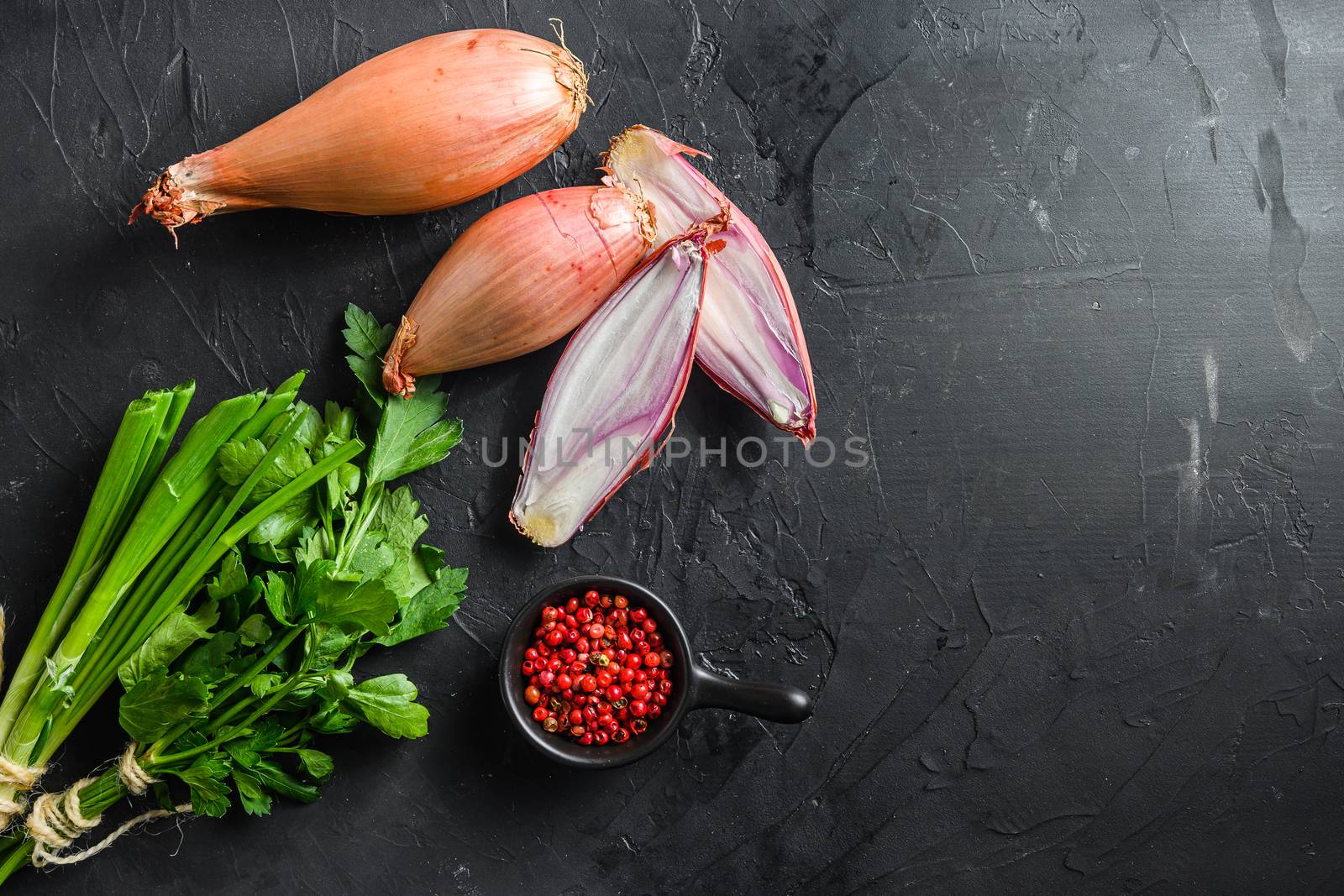 Shallot, eschalot or scallion raw ripe onions with greens and rose peppercorns sliced and halved black concrete textured background top view space for text by Ilianesolenyi