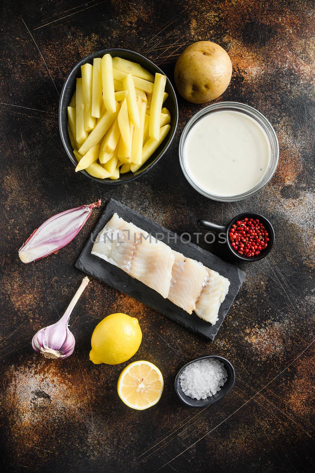 Raw cod fillet and other organic ingredients recipe fish and chips and beer batter, potatoe, shallotgarlic, salt, peppercorns on rustic metal textured surface or table top view by Ilianesolenyi