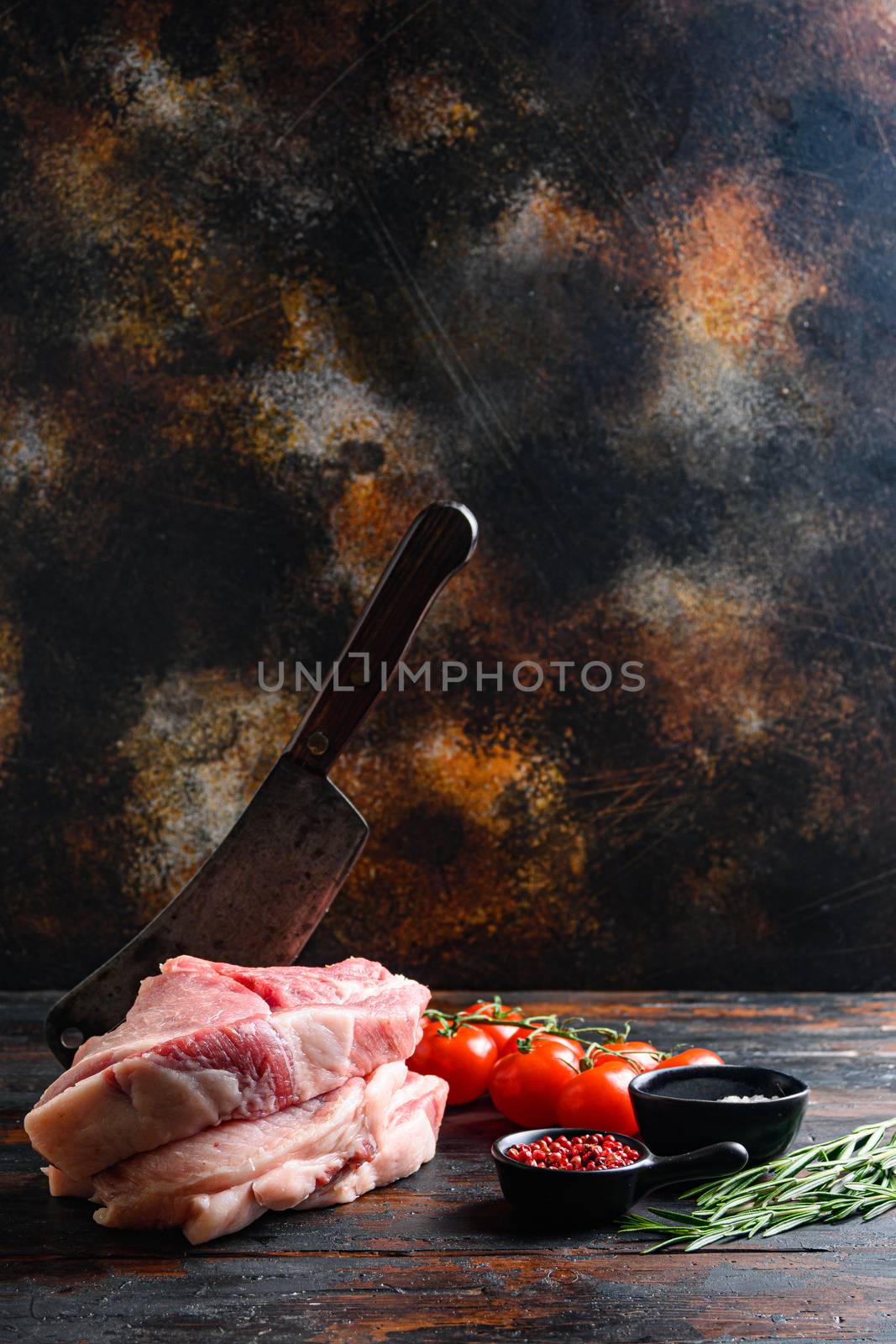 Pair organic raw pork chops arranged for cooking over wooden table and rustic backdrop and chopping cleaver butcher knife, side view spacr for text vertical.