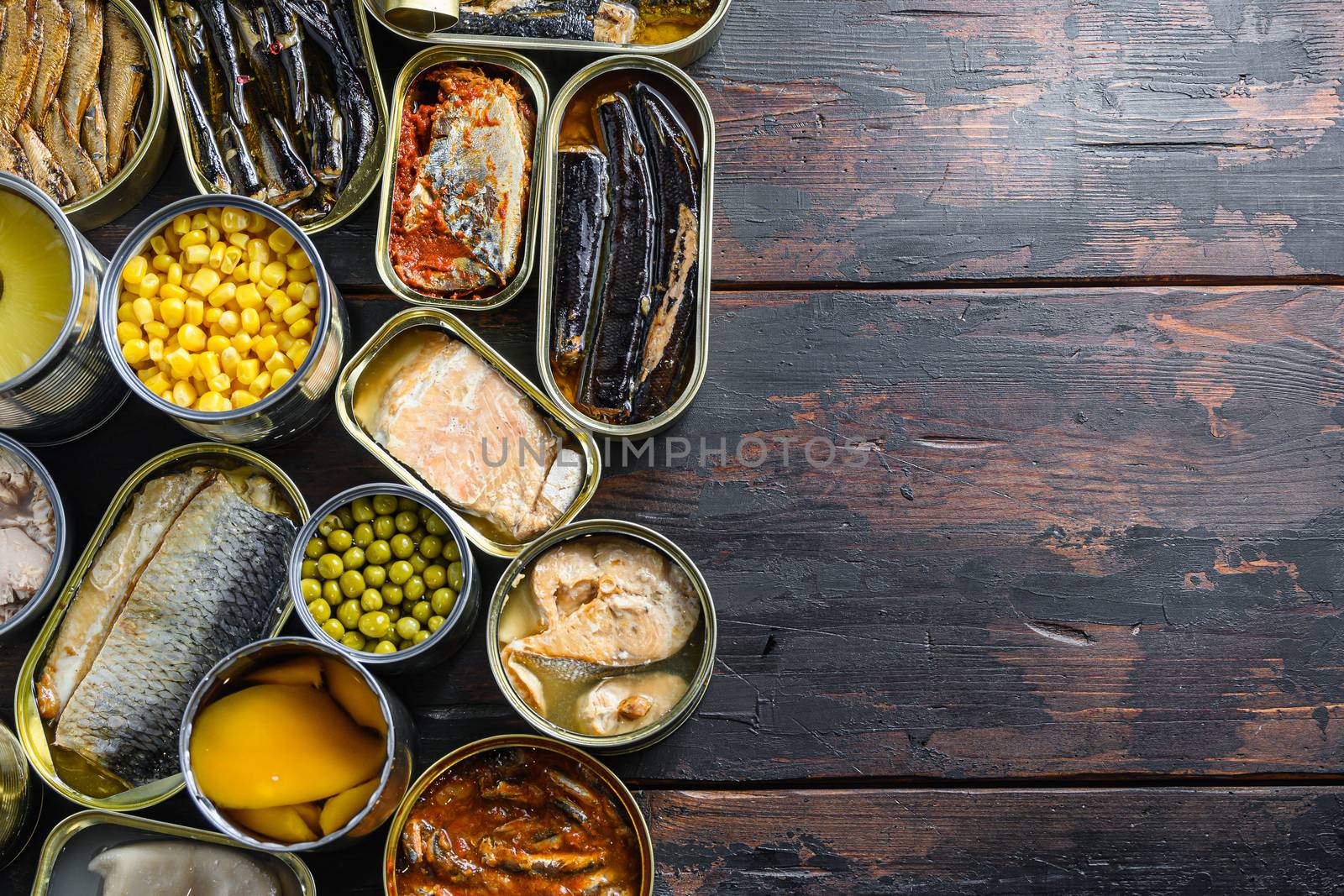 Canned preserves food in tin open cans. with fresh organic ingridients Saury, mackerel, sprats, sardines, pilchard, squid, tuna pinapple, corn, peas, mango , beans, over old wood dark textured background top view space for text.