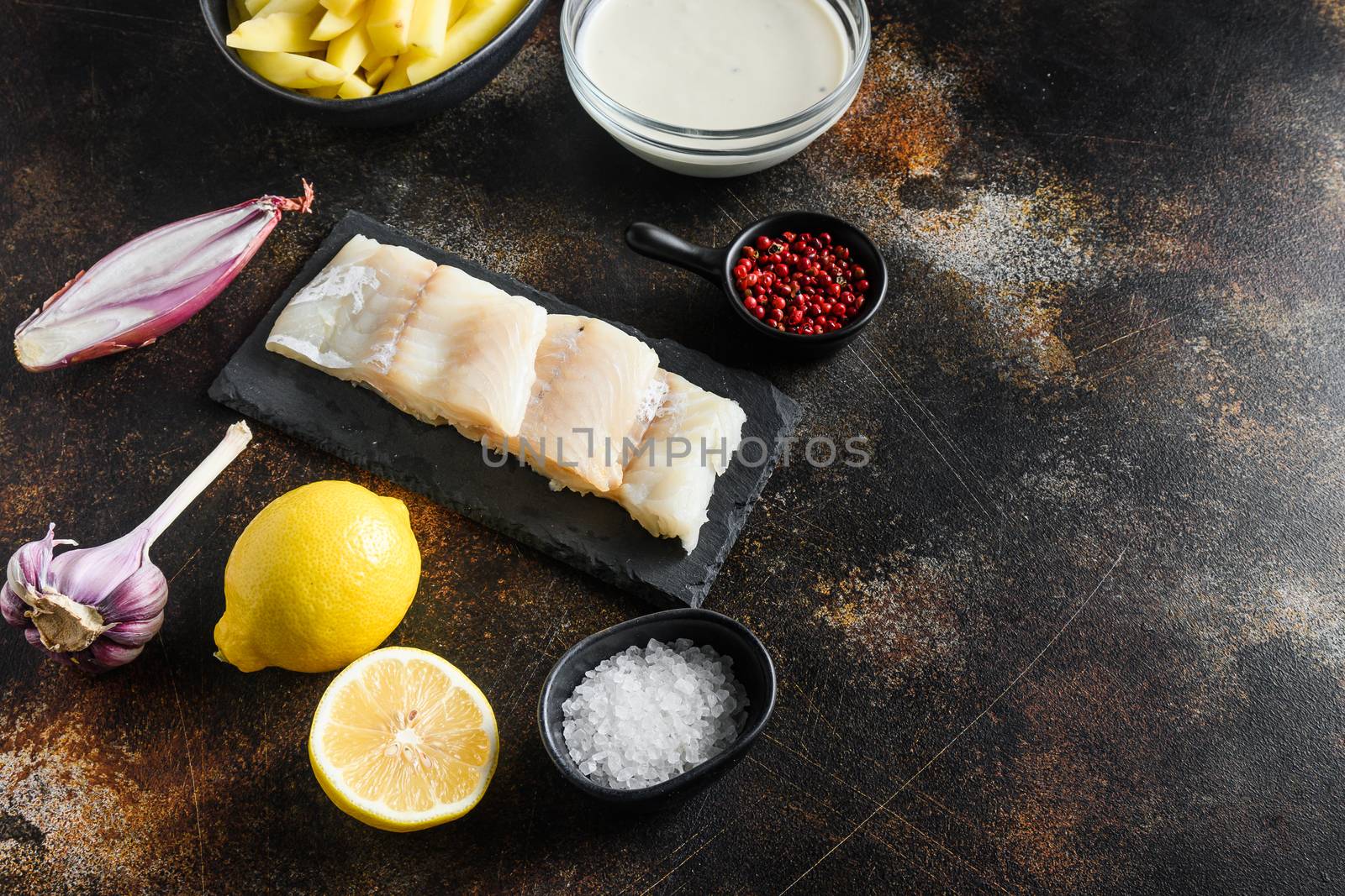 Traditional English Food such as Fish and Chip ingredients raw fish fillet, beer batter, potatoe, shallotgarlic, salt, peppercorns on rustic metal textured surface or table side view space for text.