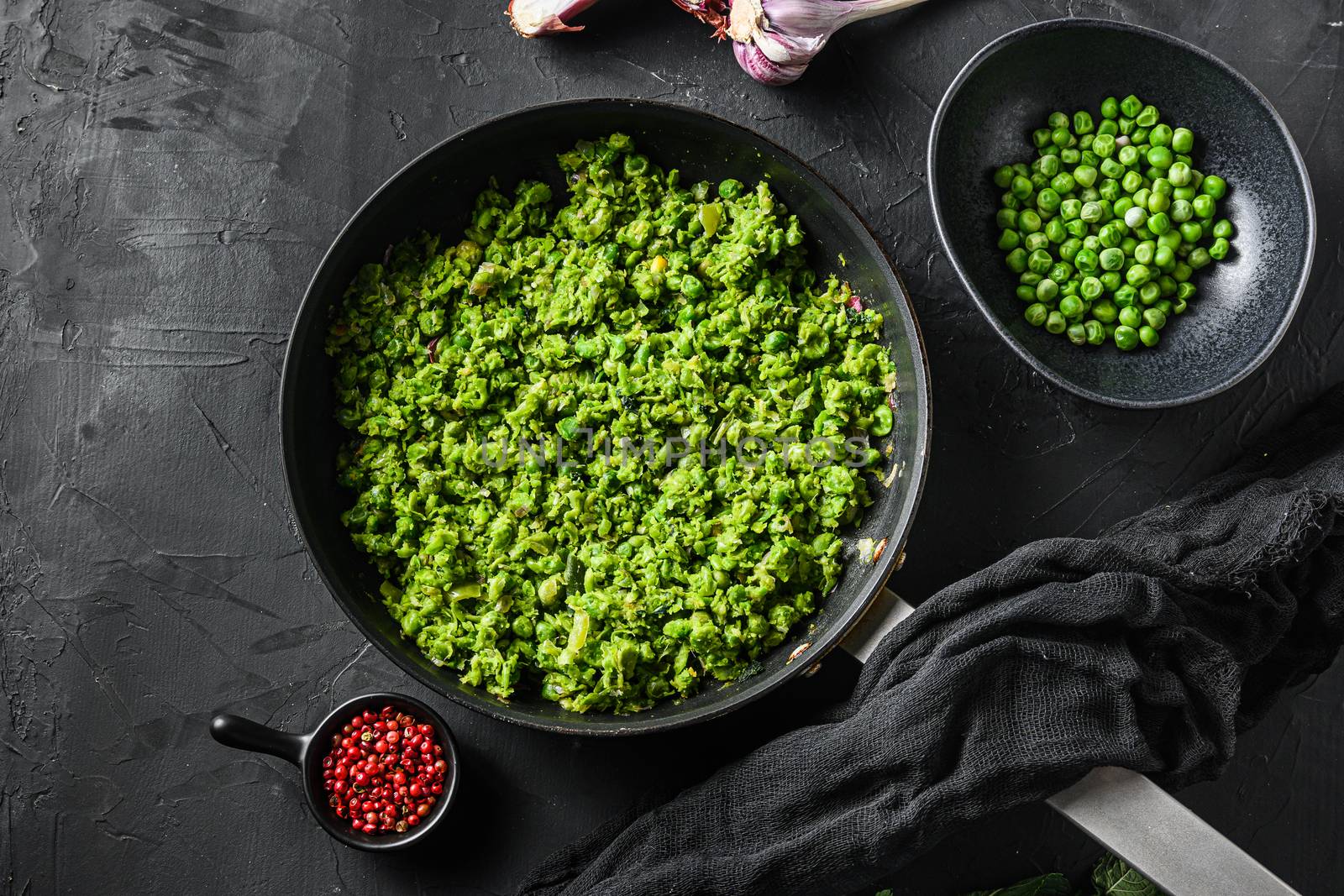 Minty mushy peass cooked frying pan and peas in bowl with mint shallot pepper and salt over black stone surface organic keto food top view by Ilianesolenyi