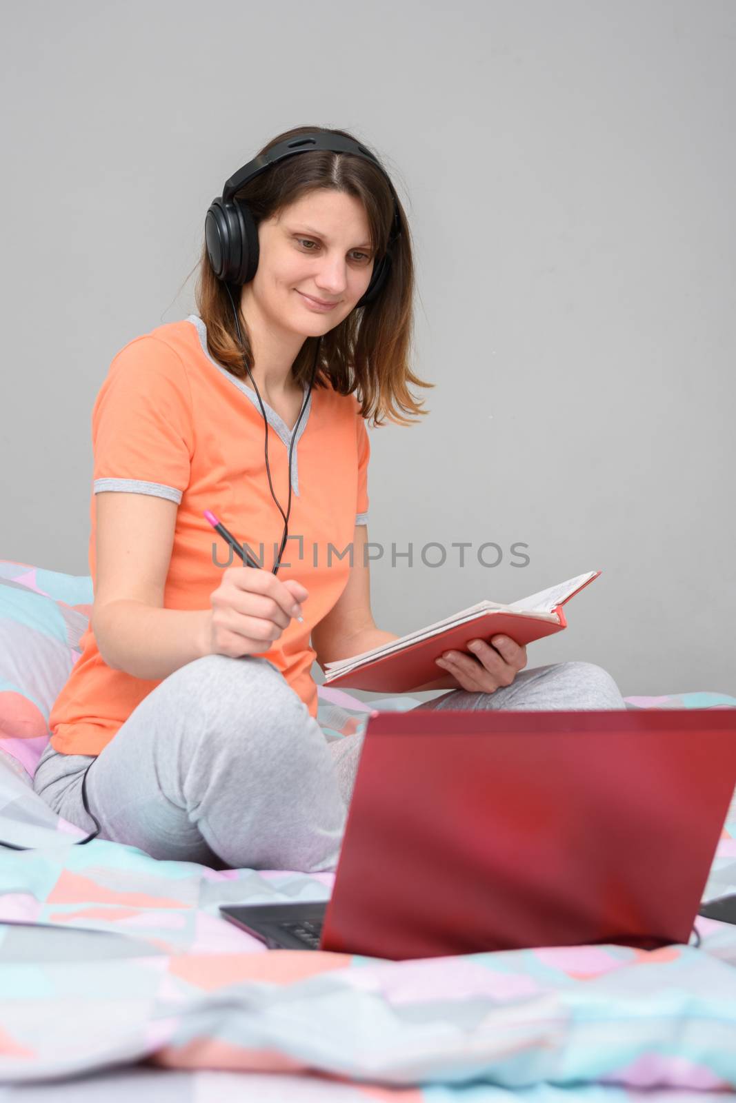 Girl is studying online sitting at home in the bed in her pajamas and wearing headphones