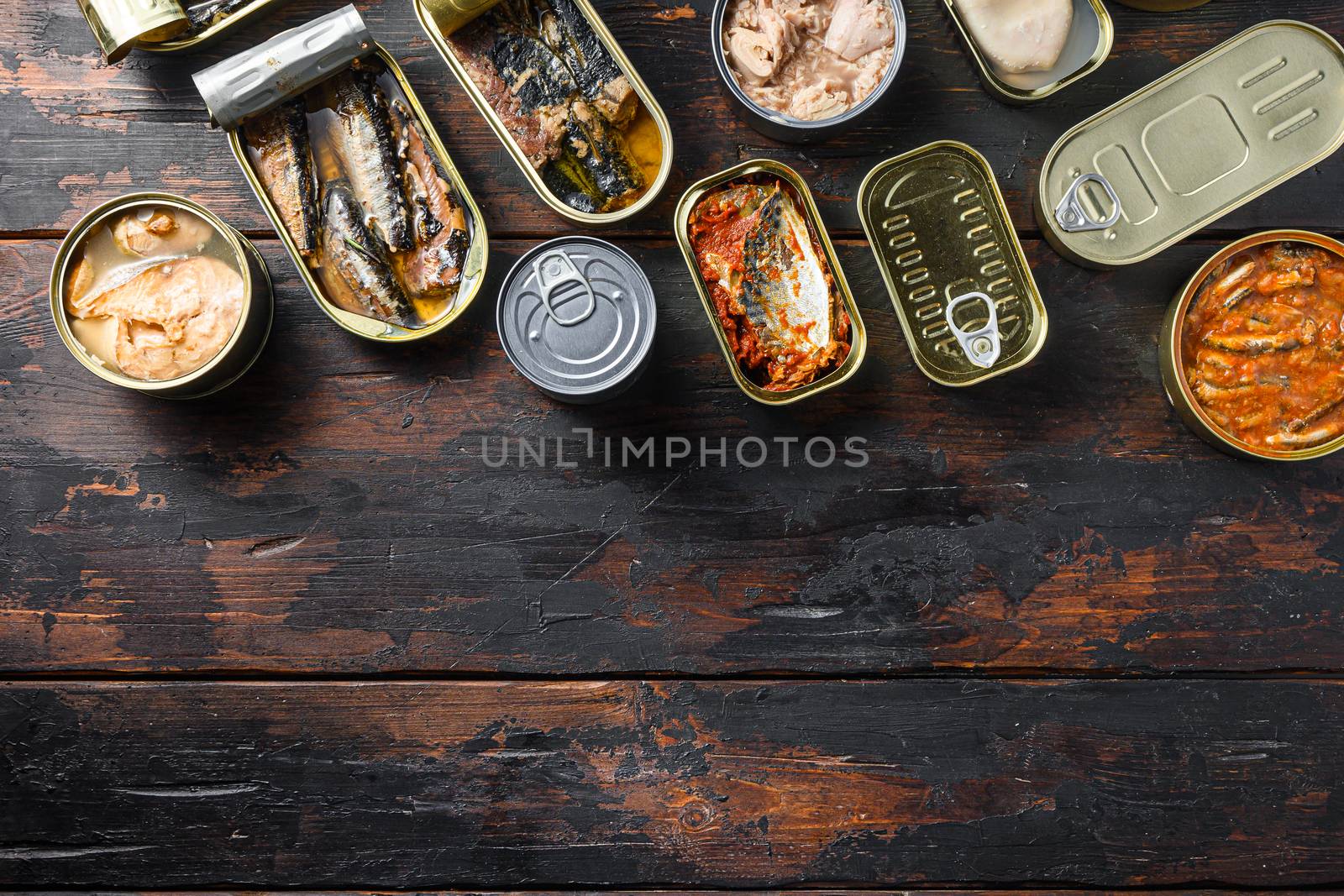 Conserves of canned fish with different types of seafood, opened and closed cans with Saury, mackerel, sprats, sardines, pilchard, squid, tuna, over dark wood old table , top view space for text.