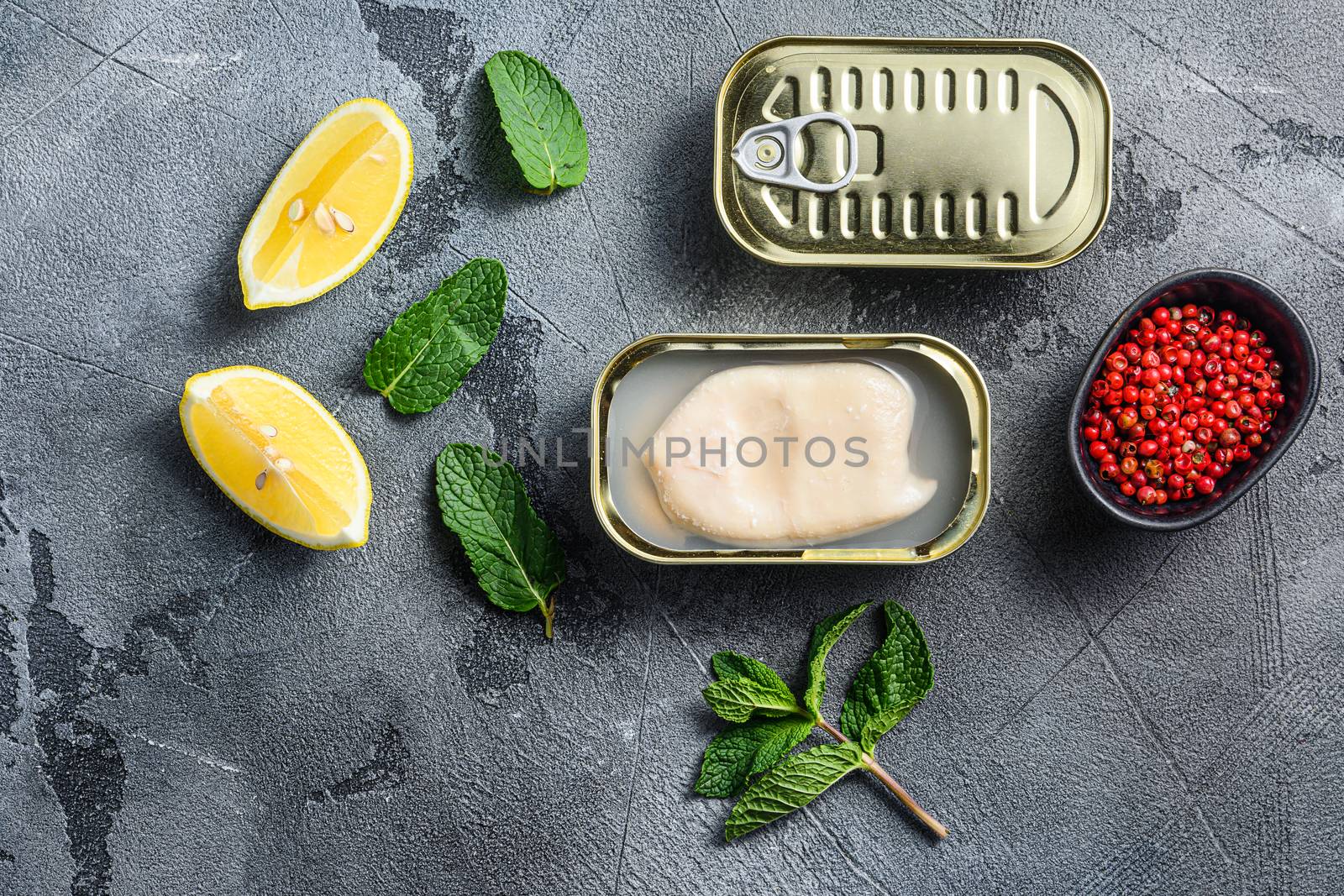 canned squid, set of opened cans closed conserve with fresh leaves and lemon with rose pepper over grey background top view .