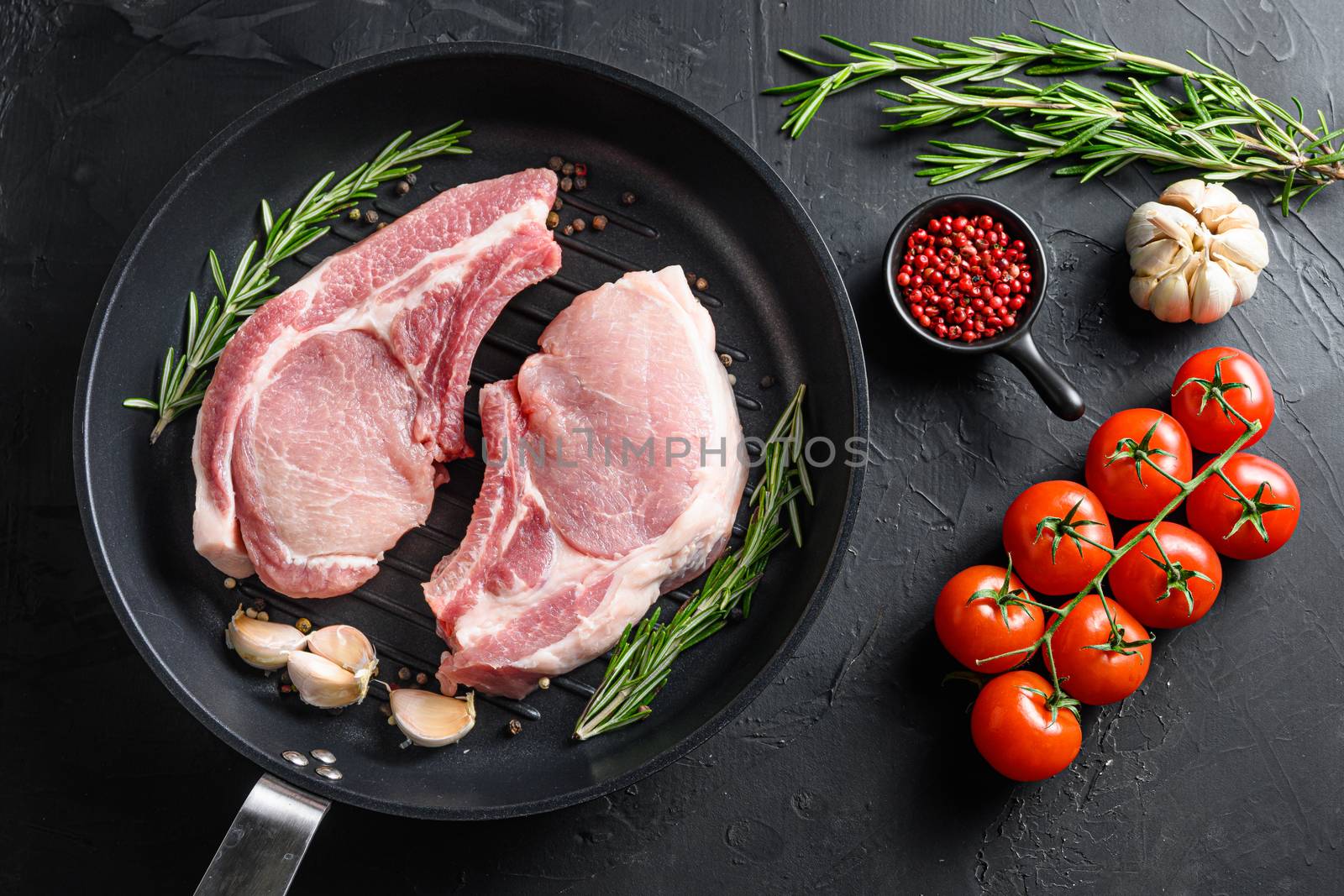 Raw Pork Loin chops in skillet near ingredients wtih herbs pepper and tomatoes top view.