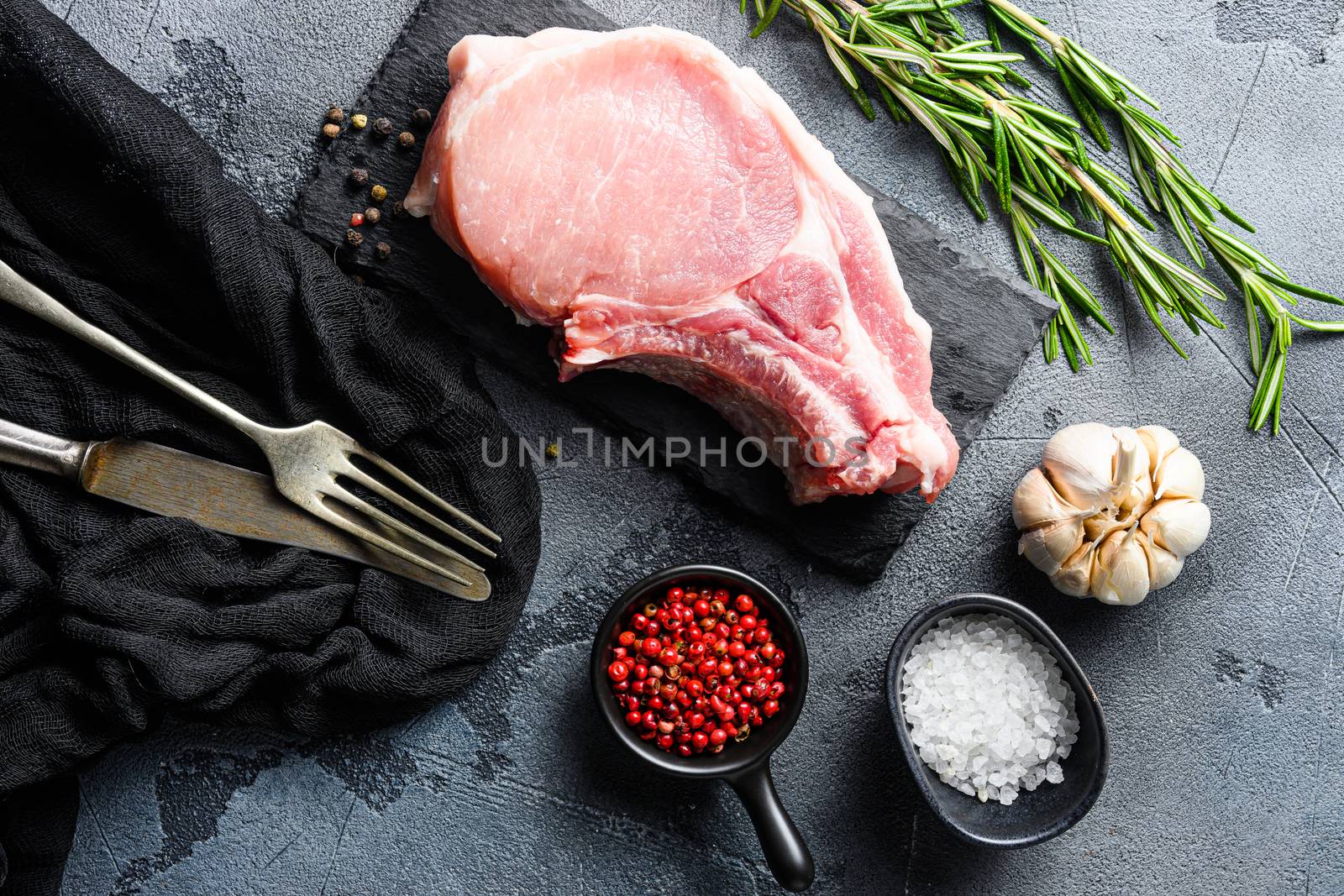 fresh raw meat with spices and rosemary and red pepper on black slate with fork and knife Top view .