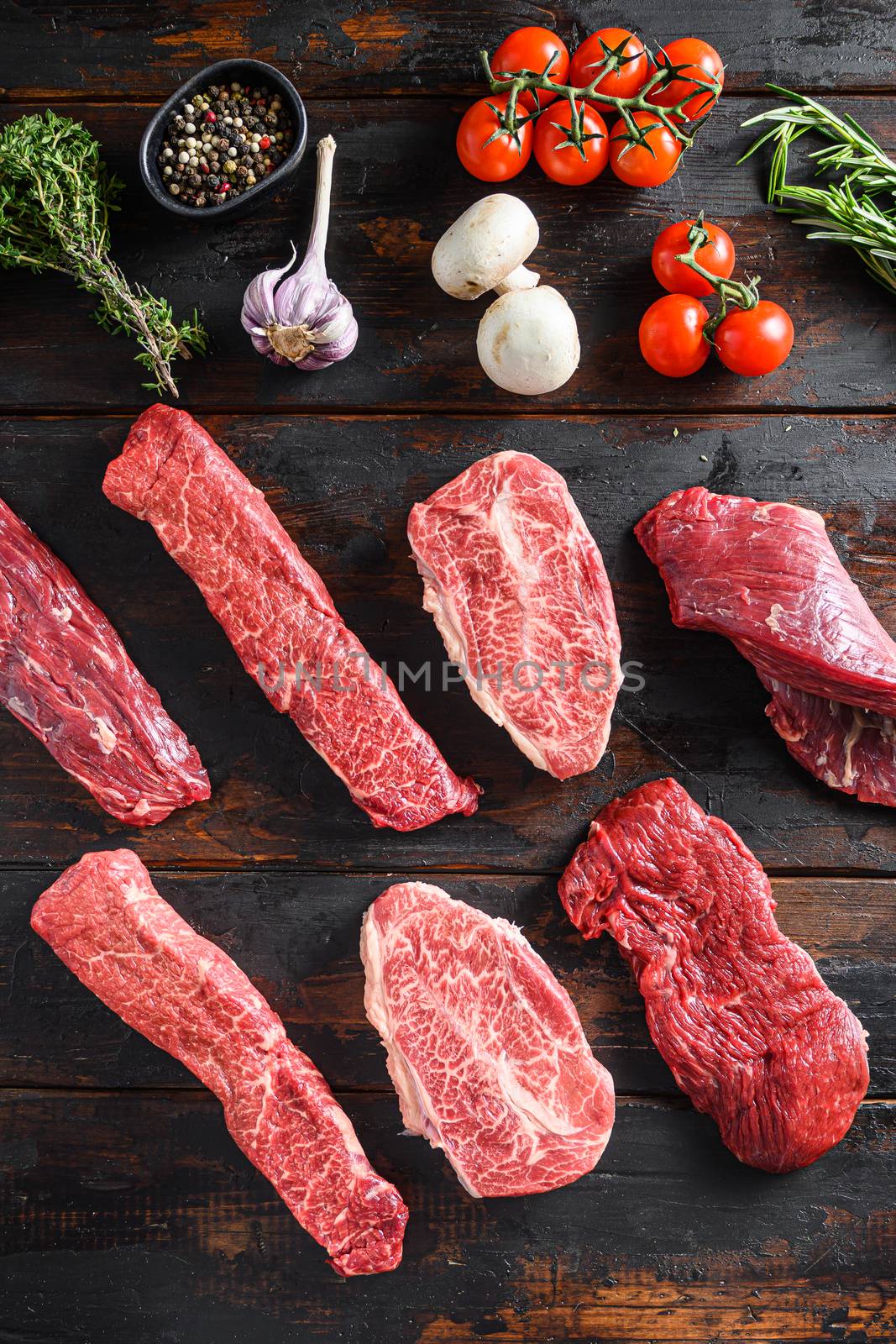 A set of different types of raw beef steaks alternative cut flap flank Steak, machete steak or skirt cut, Top blade or flat iron beef and tri tip, triangle roast with denver cut with fresh organic herbs over wood background top view vertical by Ilianesolenyi