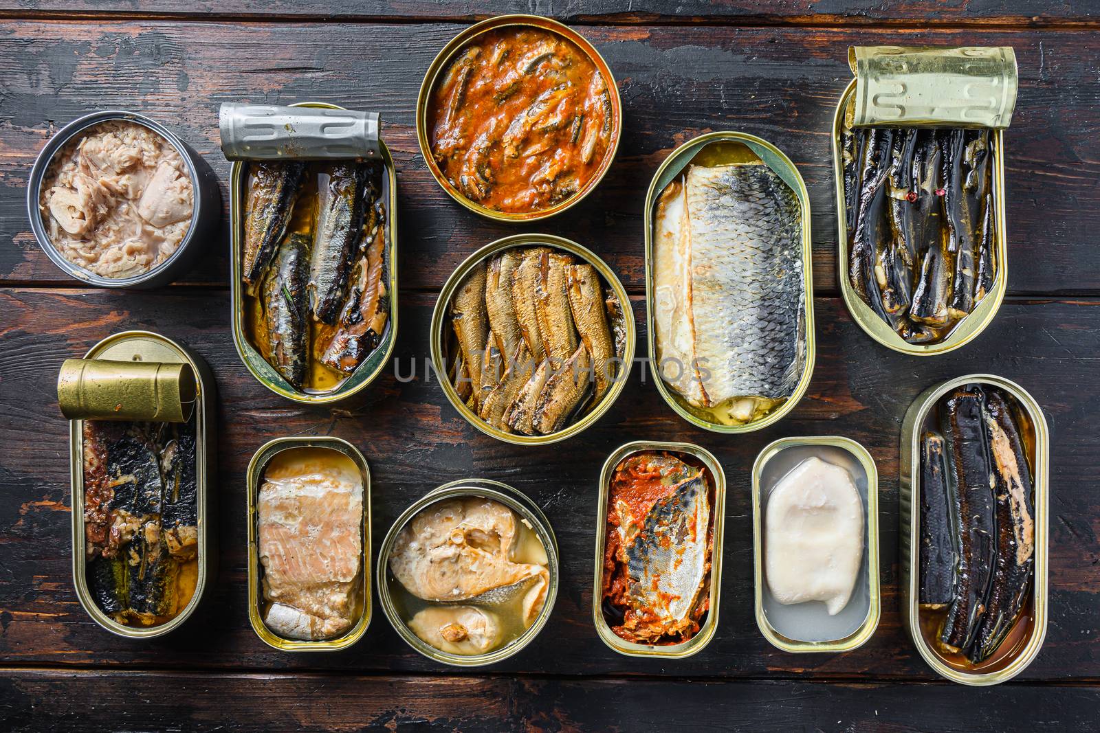 Top view of opened cans with Saury, mackerel, sprats, sardines, pilchard, squid, tuna over vintage pub wood table .