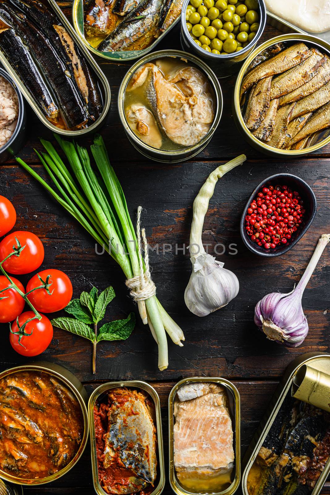 Canned preserves food in cans with fresh organic bio ingredients tomatoe herbs lemon prepared vegetables, meat, fish and fruits in tin cans On the old dark wood farm table vertical by Ilianesolenyi