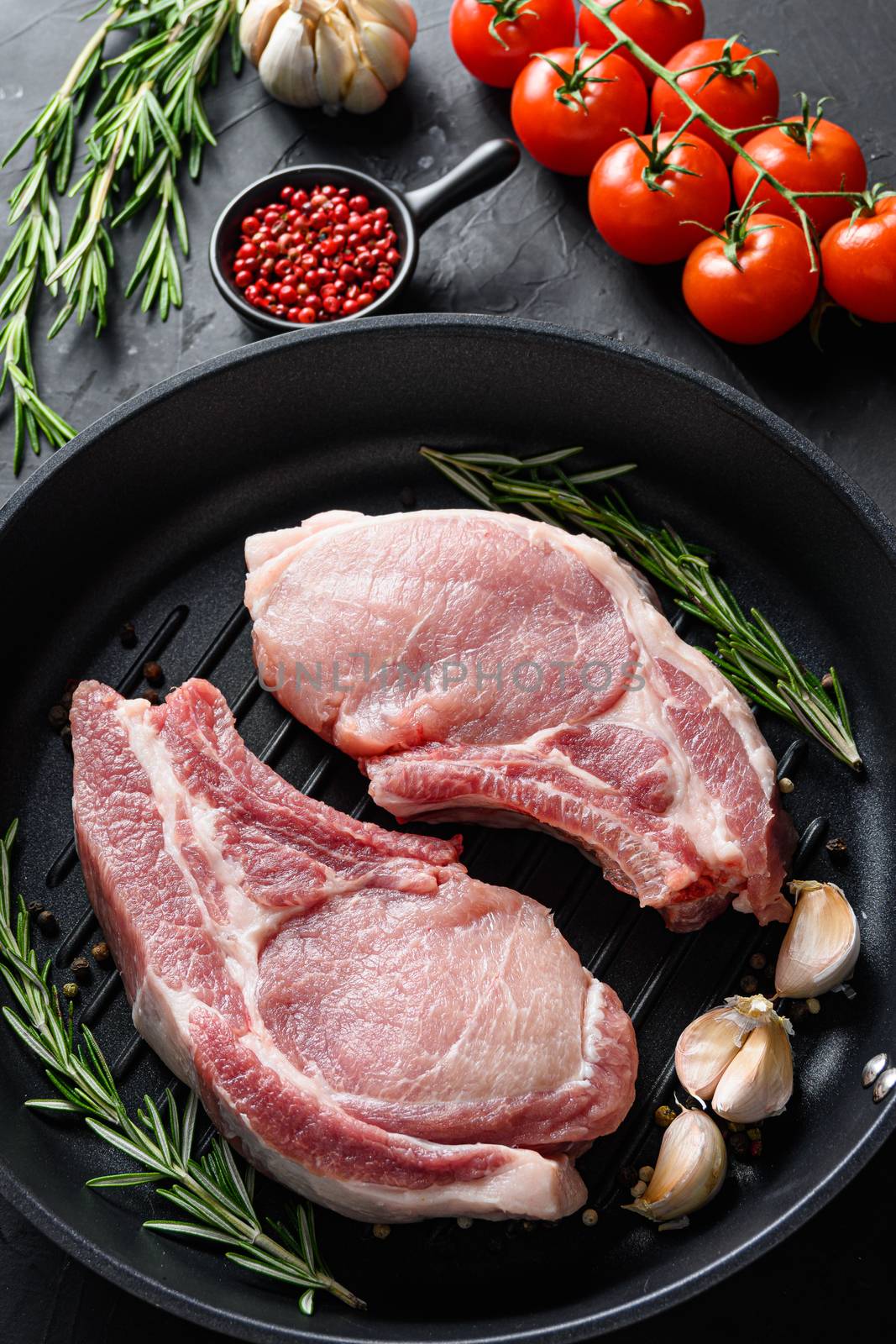 Raw Pork Loin chops in skillet near ingredients wtih herbs pepper and tomatoes top view vertical selective focus by Ilianesolenyi