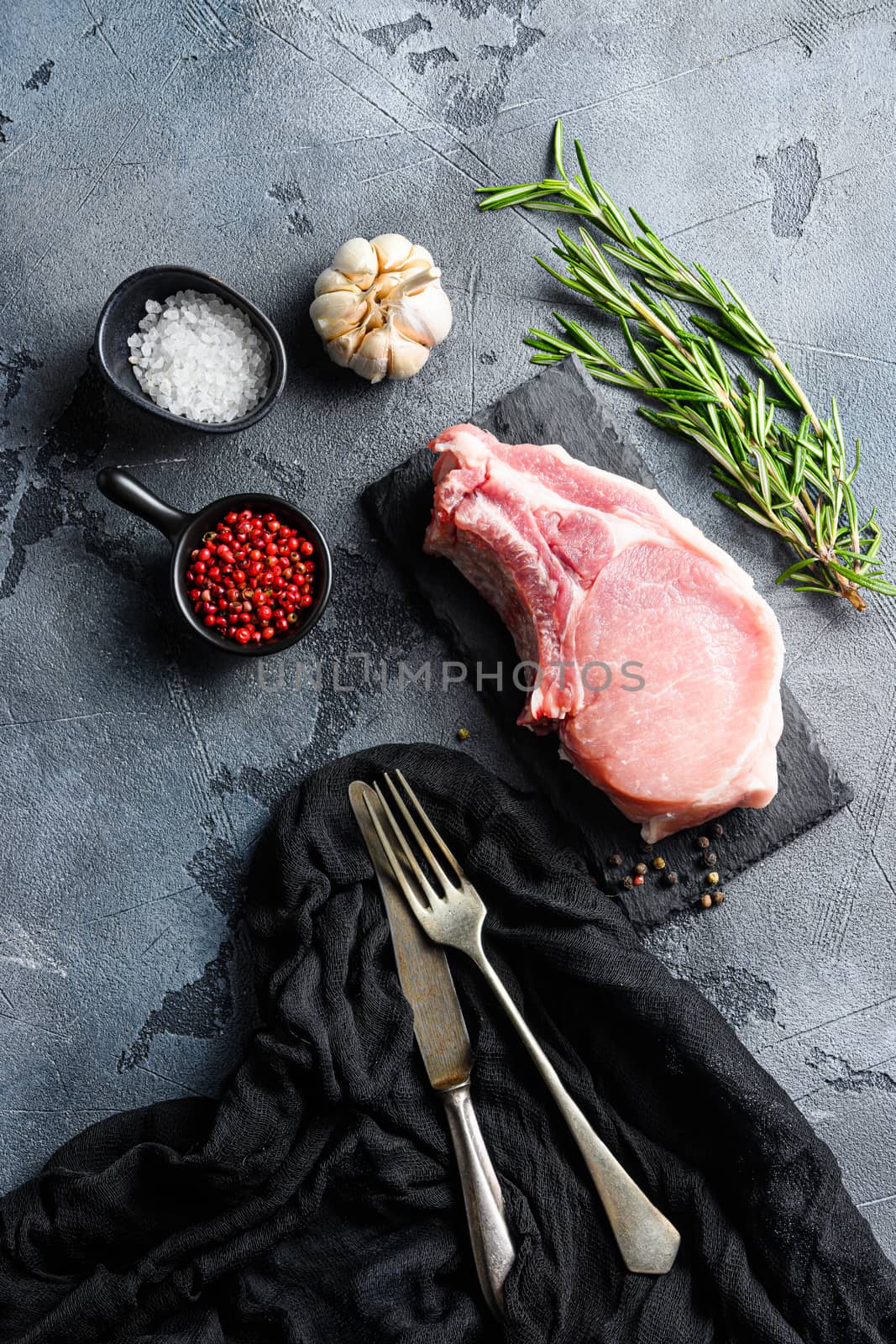 Pork chopes with herbs, spices on black slate over grey background top view
