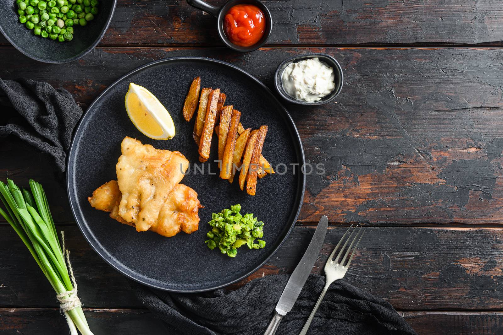 Fish chips with dip and lemon black plate with British traditional cusine food with beer-battered cod and fries and a side of tartar sauce mushy minty peas served in the Pub or Restaurant space for text by Ilianesolenyi