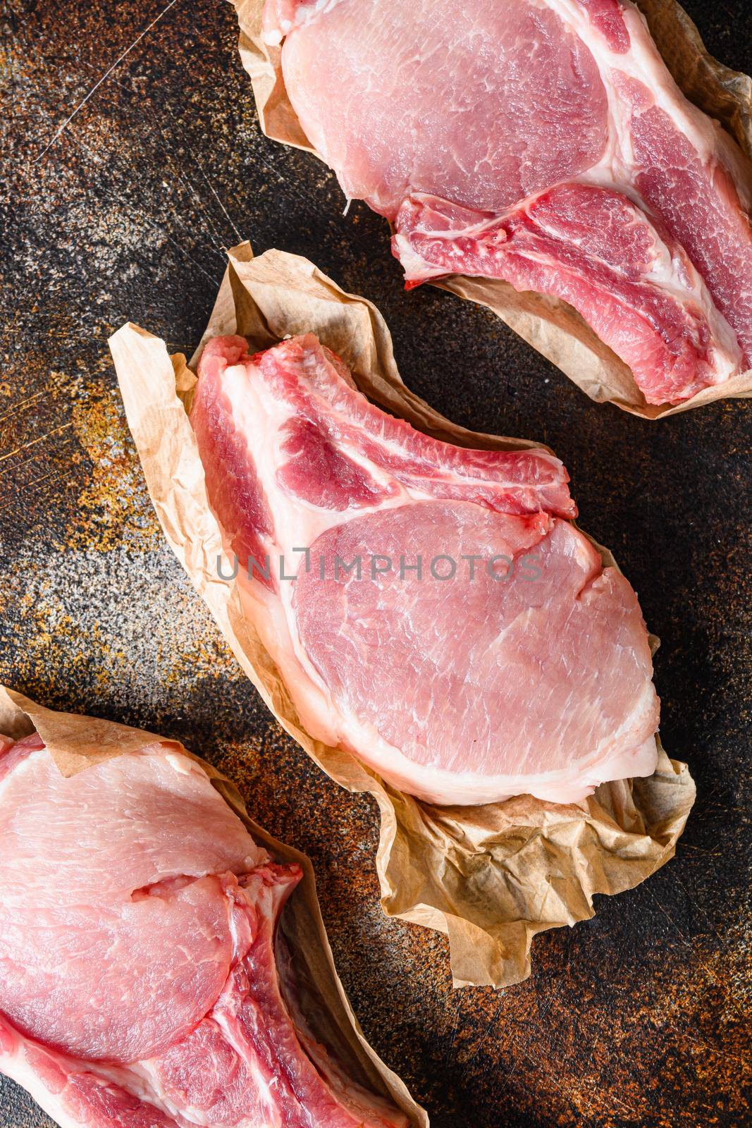 Raw pork loin chops shot from above on craft paper over rustic old metal background stock photo.