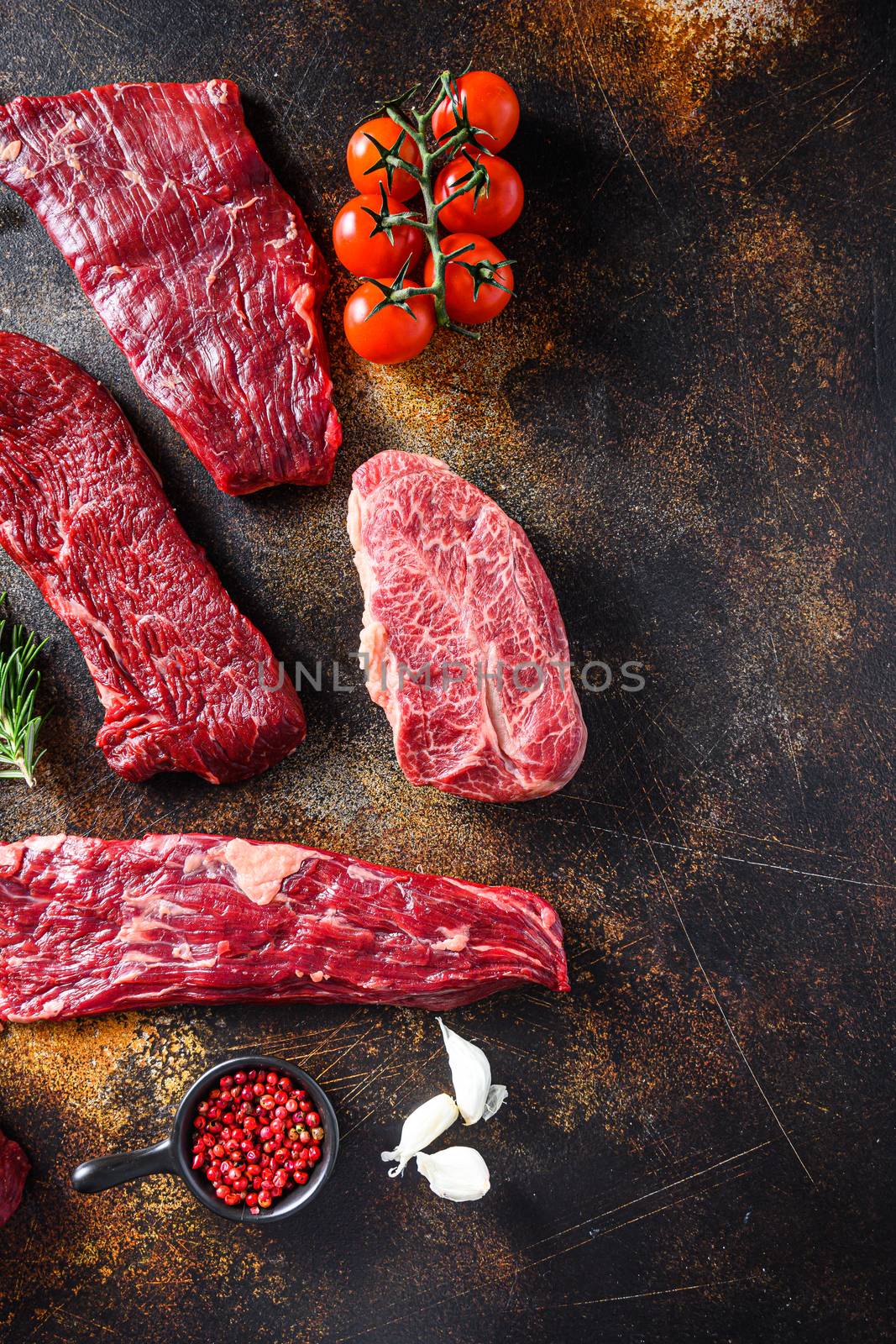 Organic set of raw alternative beef steaks flap flank Steak, machete steak or skirt cut, Top blade or flat iron beef and tri tip, triangle roast with denver cut side view over old rustic metal surface space for text on side.