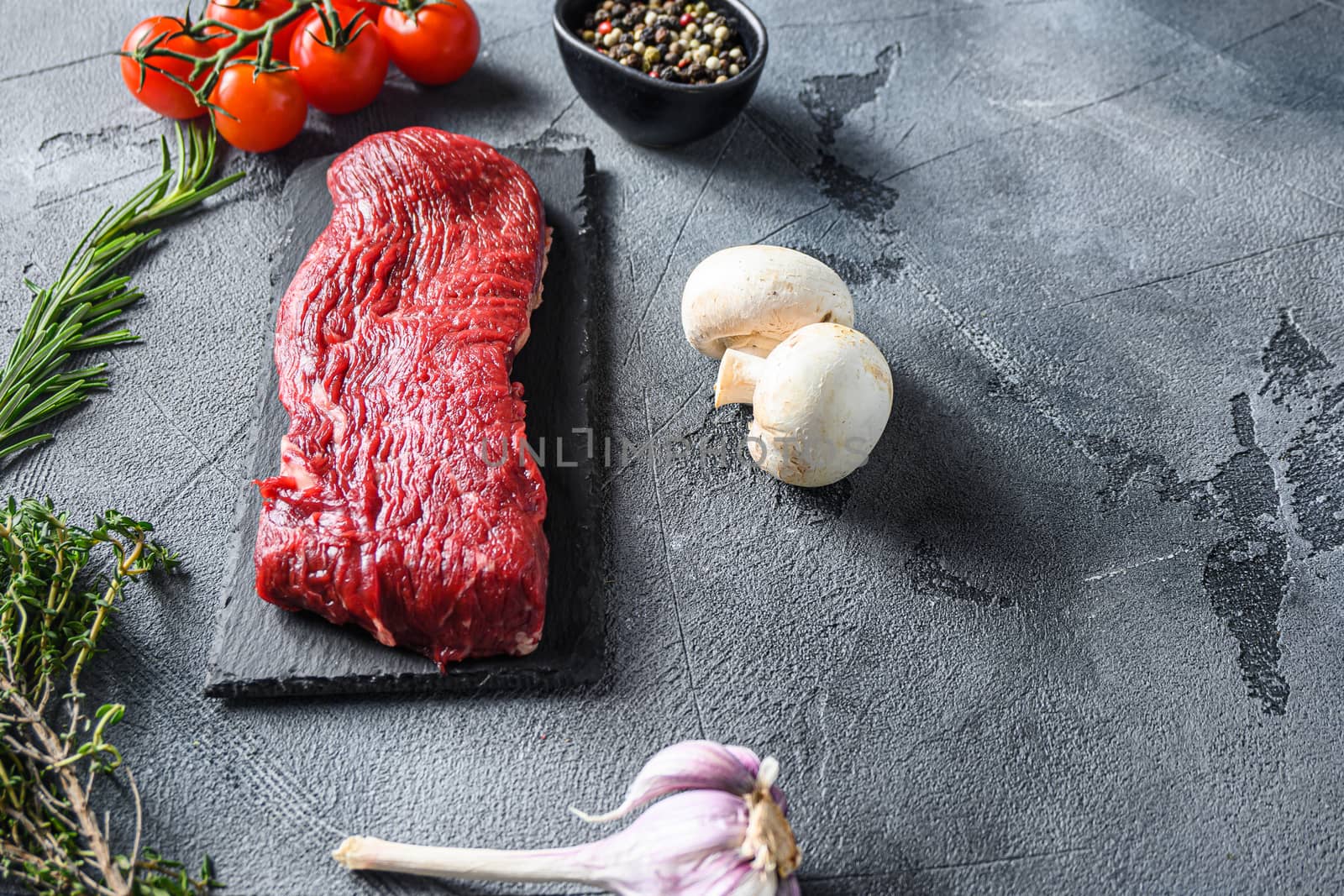 Organic Tri-tip, triangle roast marbled beef on black plate , marbled beef with herbs tomatoes peppercorns over grey stone surface background side view space for text new wide angle by Ilianesolenyi