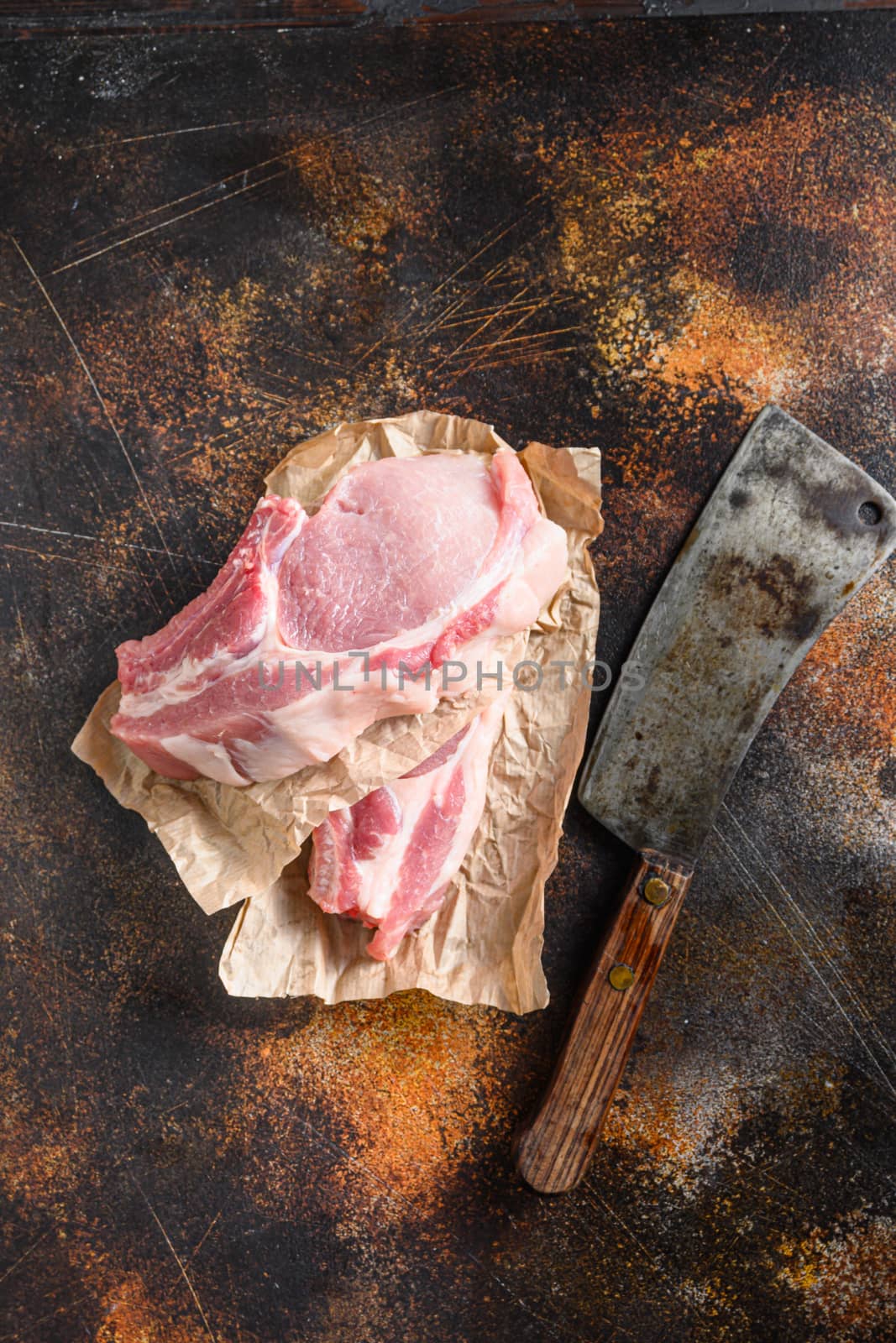 Raw pork chop warped in paper with butcher cleaver inside over rustic metall table top view vertical by Ilianesolenyi