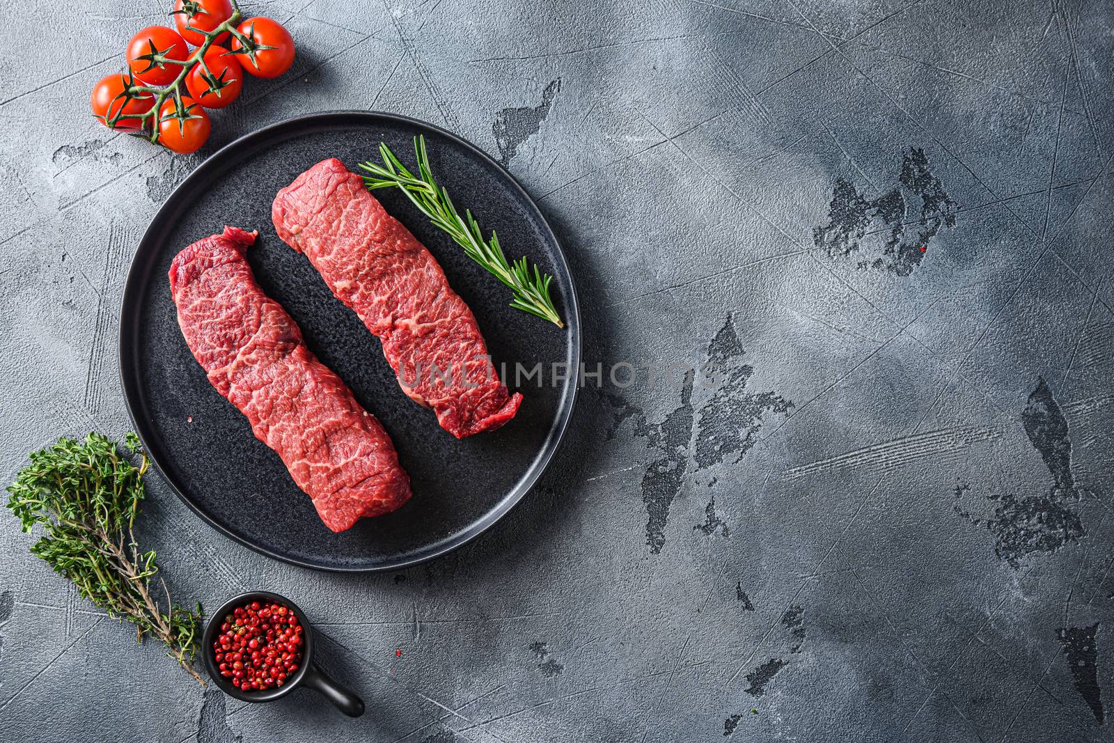 Organic denver steak on black plate , marbled beef with herbs tomatoes peppercorns over grey stone surface background top view space for text. by Ilianesolenyi