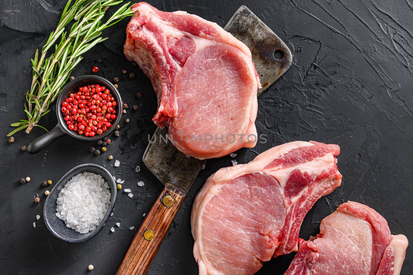 Raw pork meat chopes with herbs and spices with meat american cleaver on black background space for text by Ilianesolenyi