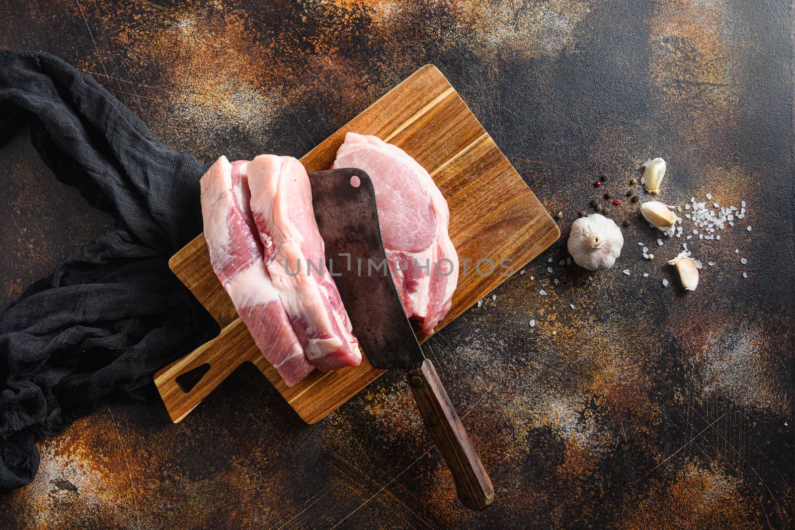 Pork belly Farm fresh , cutlet on a choppong board with butcher knife cleaver in meat on a old rustic dark metall surface rosemary garlic peppercorns top view space for text.