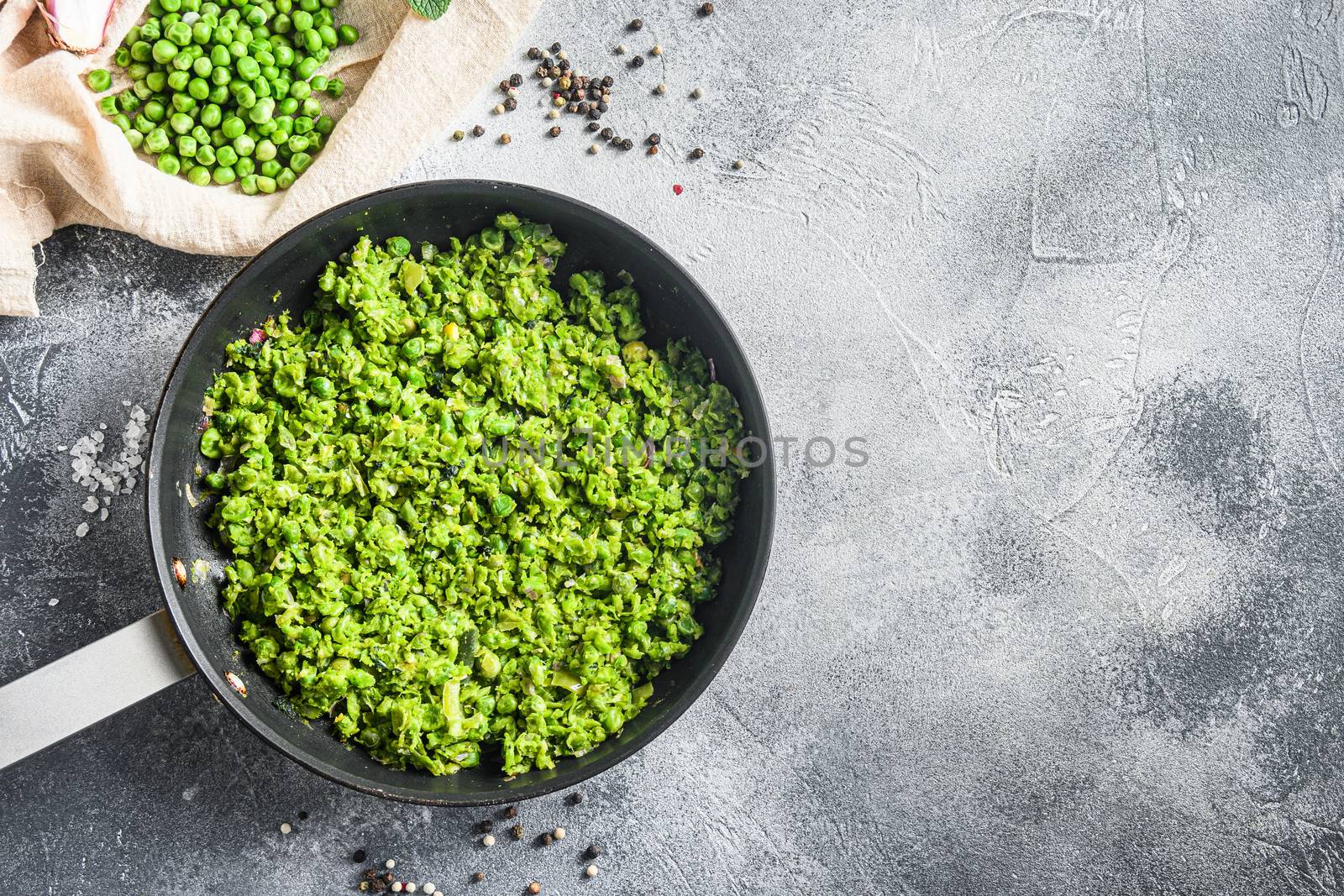 British mushy peas cooked frying pan and peas in bowl with mint shallot pepper and salt over grey stone surface organic keto food overhead photo space for text.