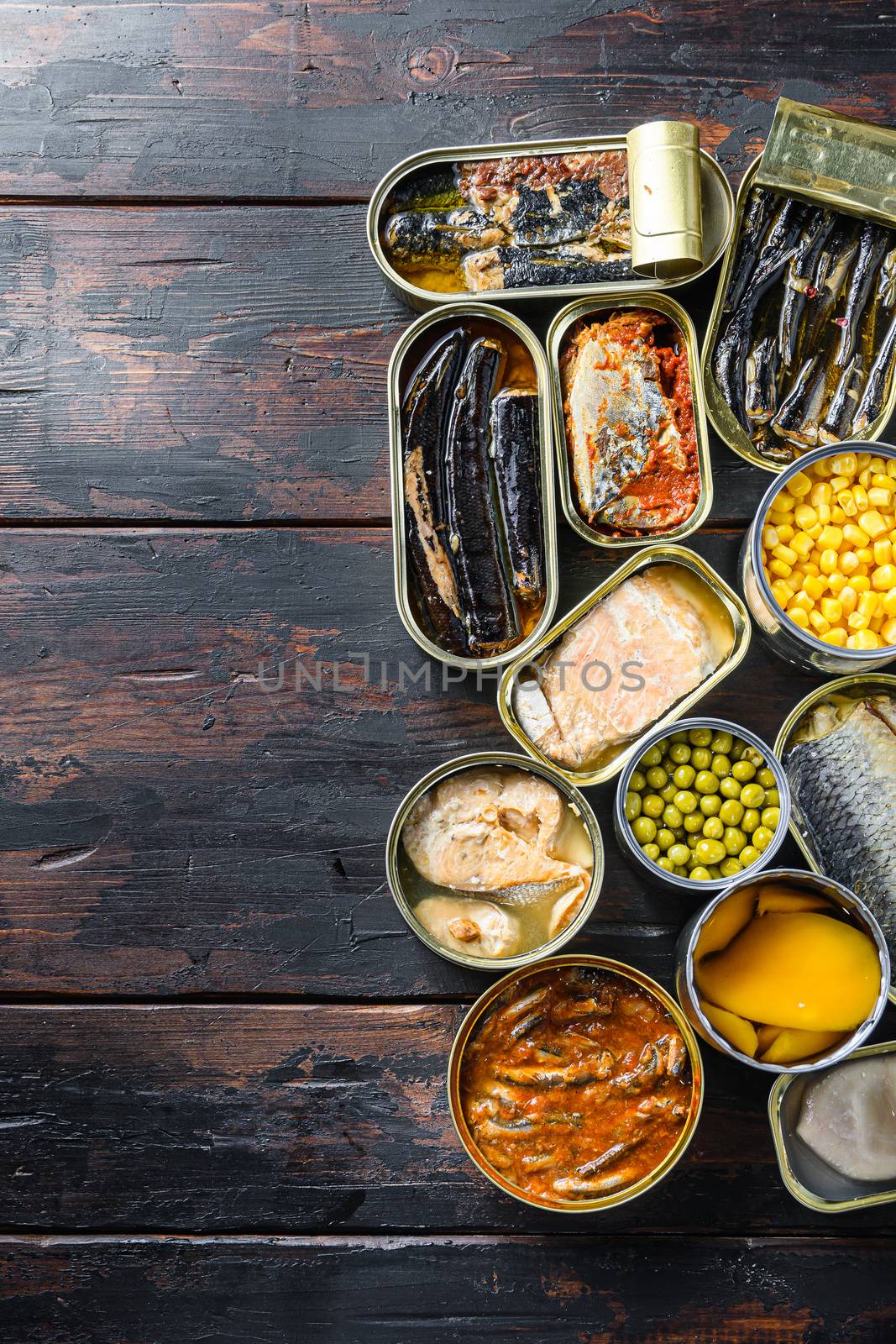 Assortment of canned preserves food in tin open cans. with fresh organic ingridients Saury, mackerel, sprats, sardines, pilchard, squid, tuna pinapple, corn, peas, mango , beans, over old wood dark textured background top view vertical space for text concept by Ilianesolenyi
