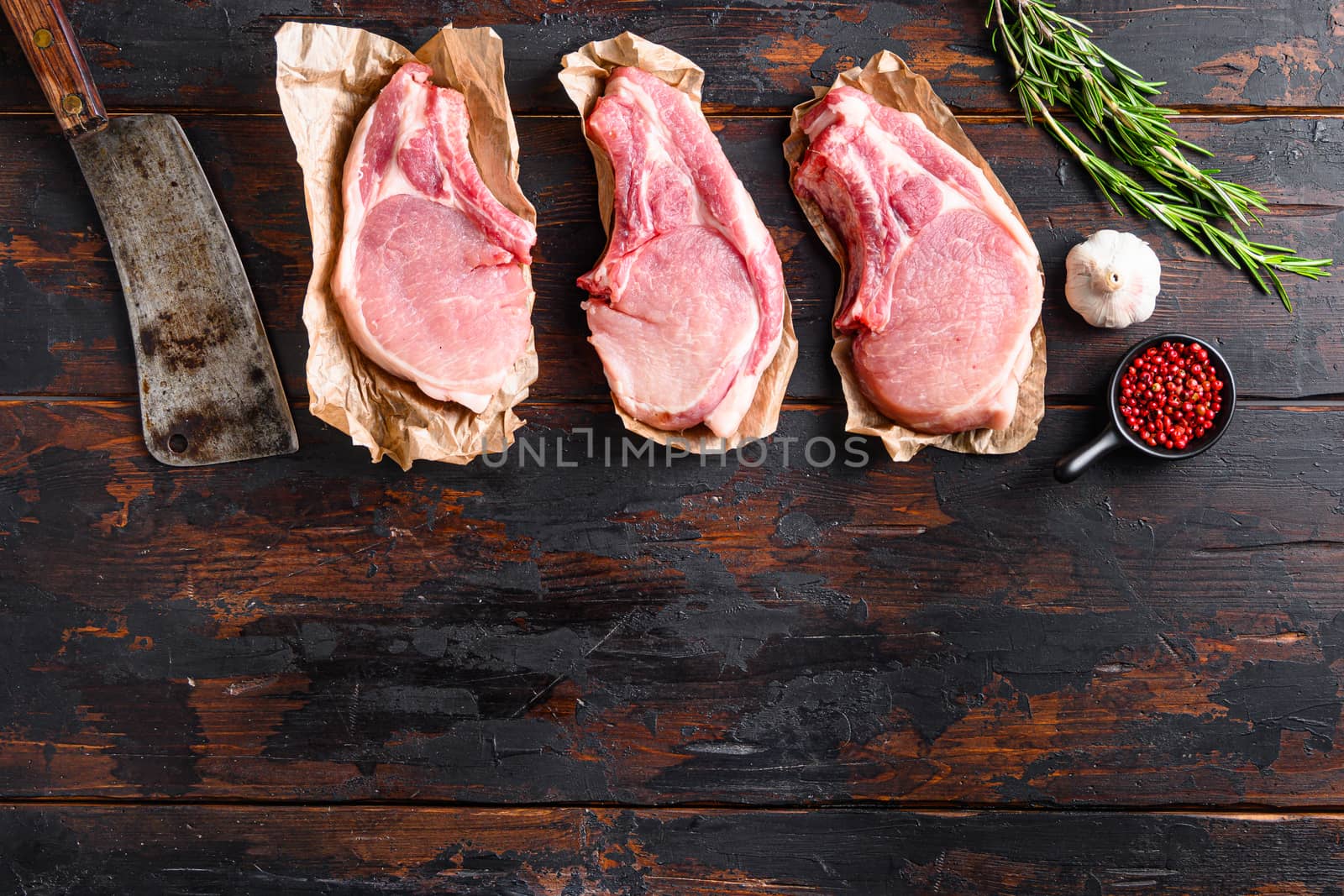 Concept organic pork meat set for grill with old american butcher knife or cleaver over old rustic dark wood table with herbs and ingrefients top view space for text. High quality photo