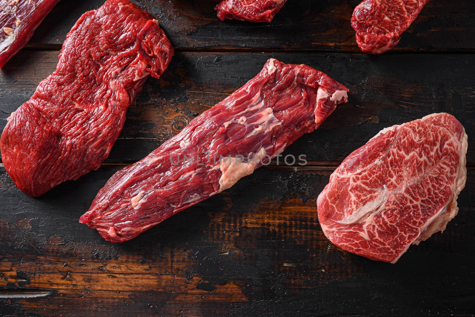 Alternative beef cut machete skirt steak near tri-tip and top blade oyster cuts close up in front of other cuts in butchery on old wood table top view .