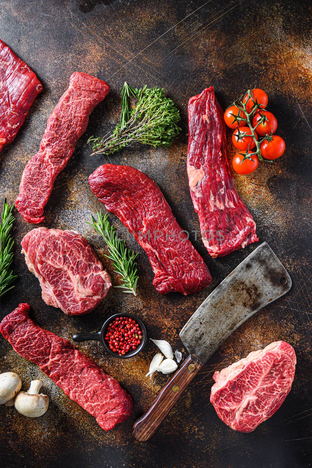 Set of different alternative types of raw beef steaks,with butcher cleaver knife on a rustic metall background top view concept frame space for text vertical.