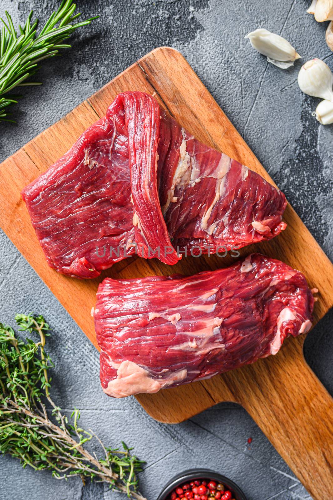 Raw flap steak flank cutHanger steak, bistro steak, fajita meat, on woods chopping board, with herbs tomatoes peppercorns over grey stone surface background top view close up by Ilianesolenyi