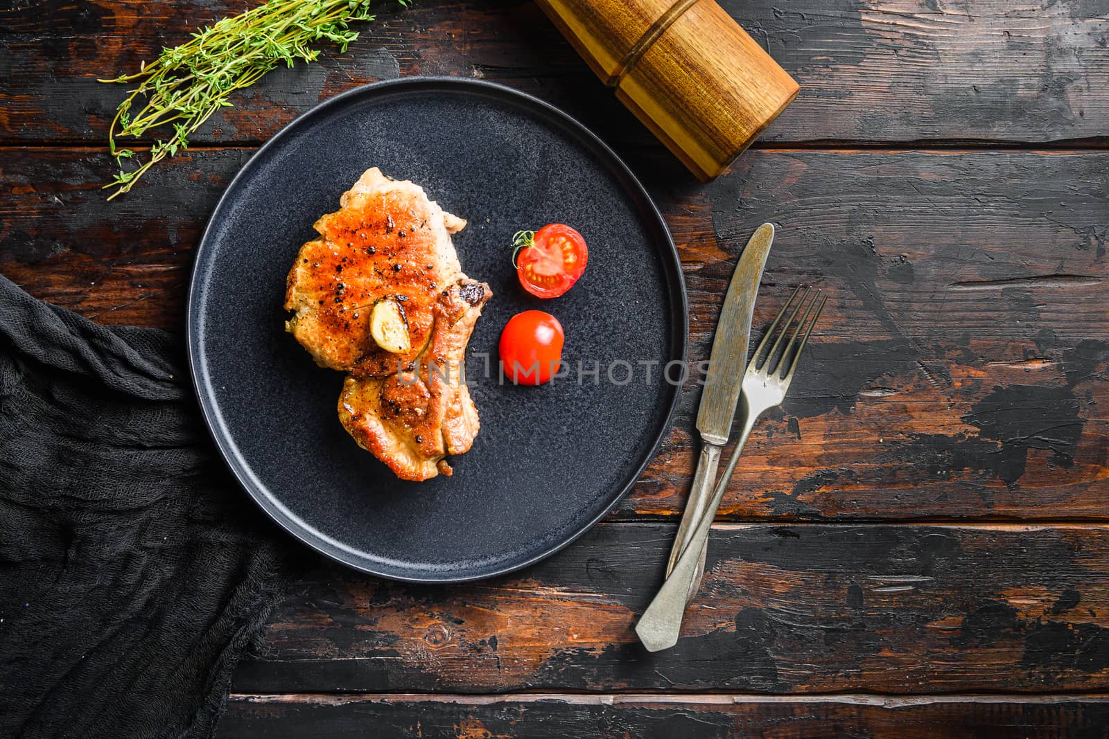 Dish of grilled pork chop with tomatoes top view with knife and fork over old rustic dark wood table table top view. Space for text.