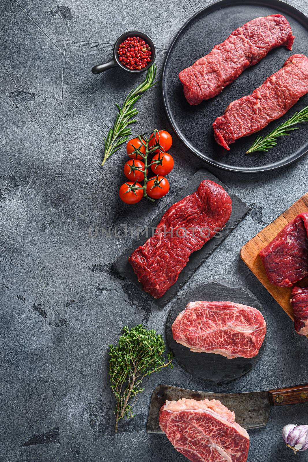 Organic denver, top blade, tri tip steak on a black plate and stone slate with seasonings, herbs grey concrete background. Top view vertical concept space for text by Ilianesolenyi