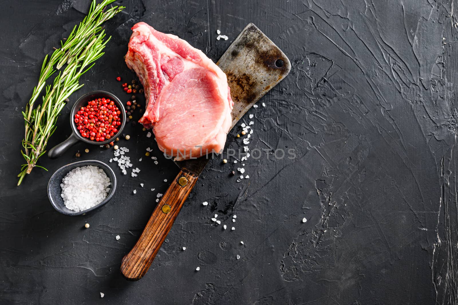 Organic cutlet on a rib or Pork meat over american classic butcher knife or cleaver with spices and rosemary and red pepper on black slate top view. Space for text.